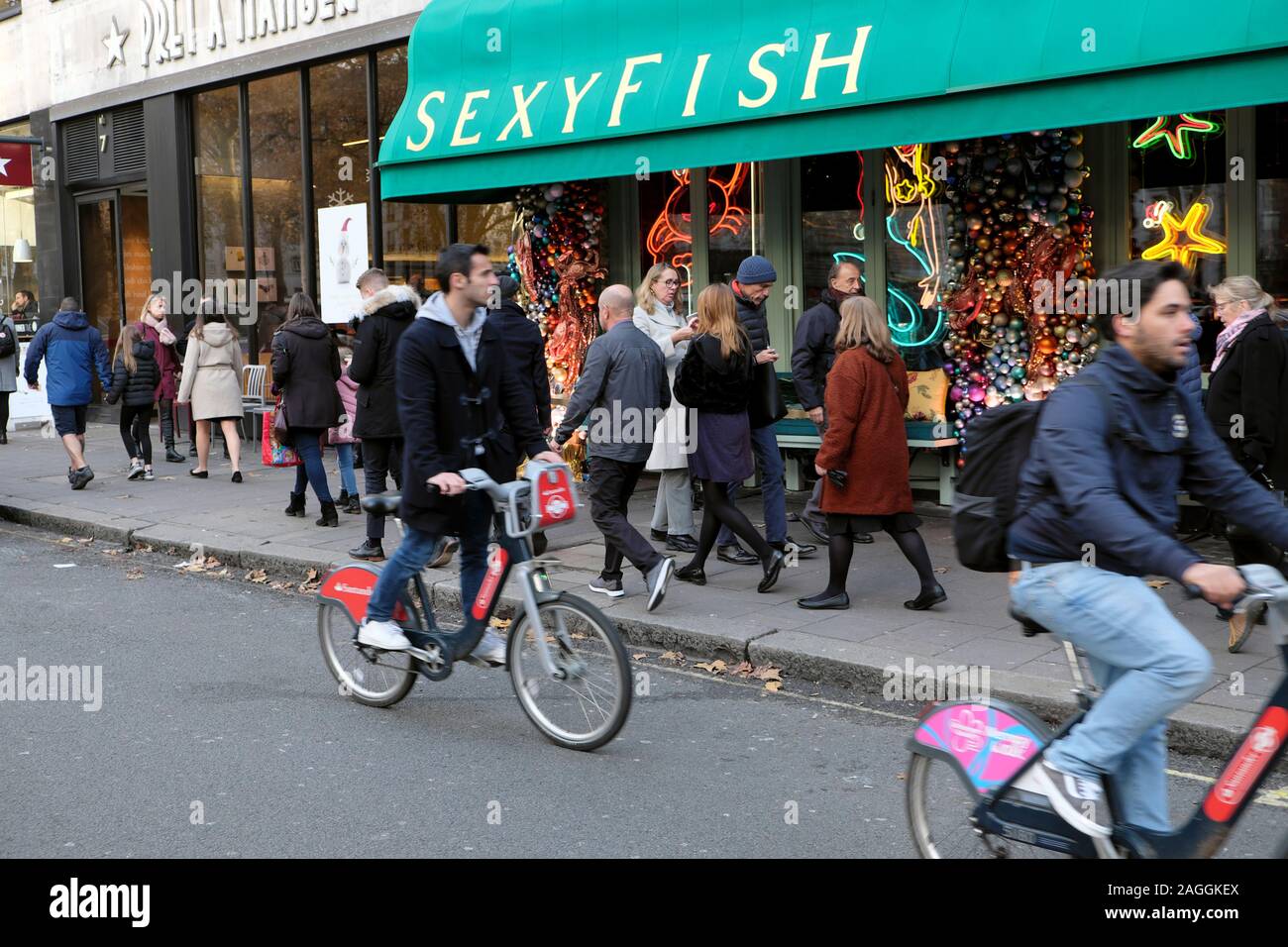 Männer Radfahren über Santander Fahrräder und Menschen zu Fuß außerhalb Sexyfish Restaurant außen in Berkeley Square London W1England UK KATHY DEWITT Stockfoto