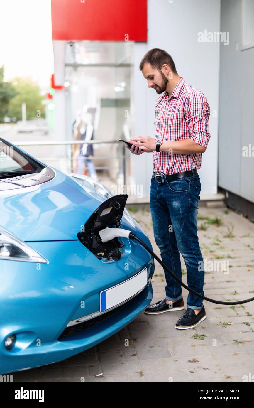 Ein Mann, der an die Stromversorgung für Elektroauto Ladestation Aufladen der Batterie des Fahrzeugs, und überprüfen Sie den Status und die Kontrolle mit der mobile Smar Stockfoto