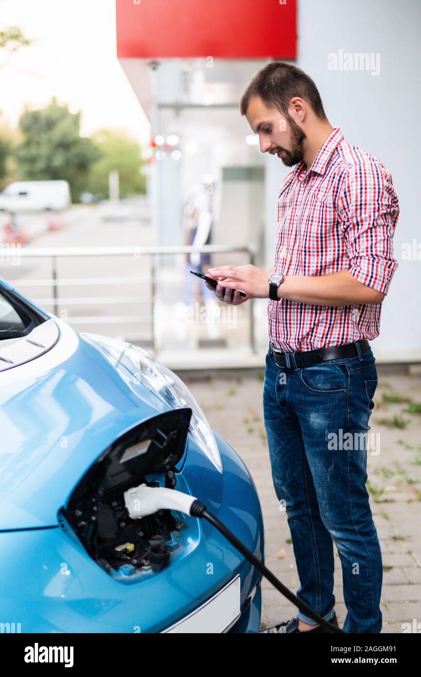 Ein Mann, der an die Stromversorgung für Elektroauto Ladestation Aufladen der Batterie des Fahrzeugs, und überprüfen Sie den Status und die Kontrolle mit der mobile Smar Stockfoto