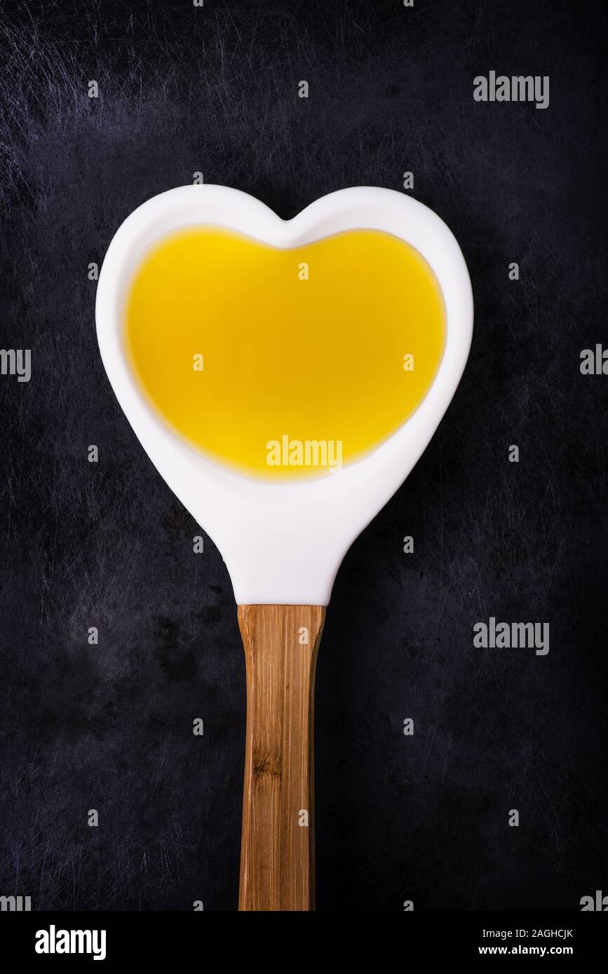 Isolierte Schöpfkelle aus der Form eines Herz voll von Olivenöl auf dem dunklen Hintergrund Stockfoto