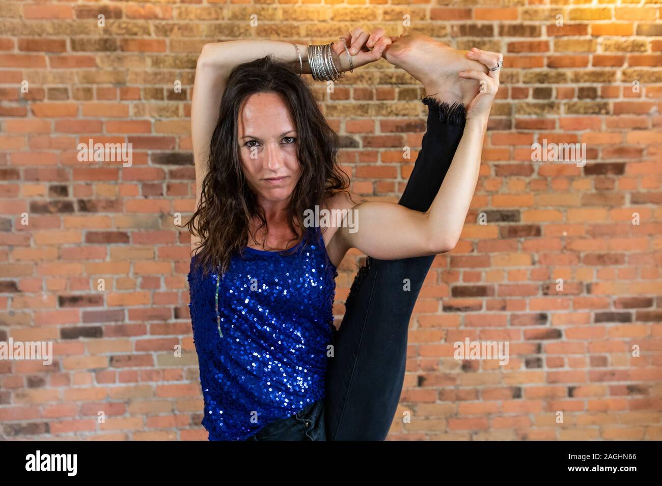 Stern suche Frau, als sie Praktiken, eine anstrengende Vinyasa Yoga Routine in einer Turnhalle gegen eine Orange und Red brick wall Stockfoto