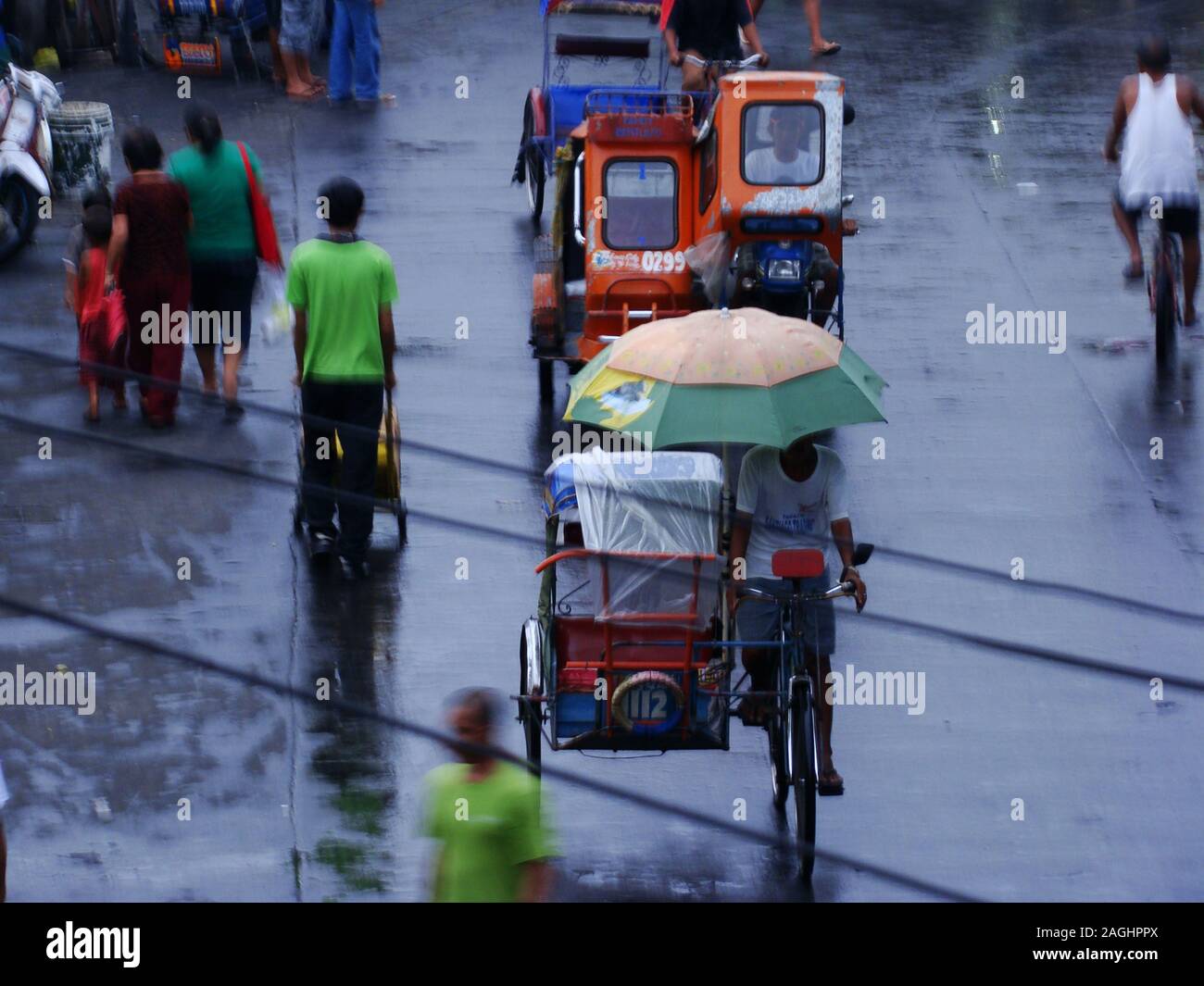 Auto-rikschas (Tuk-tuks) und Passanten an einem regnerischen Tag in den Straßen von Tabaco City, Luzon, Philippinen Stockfoto