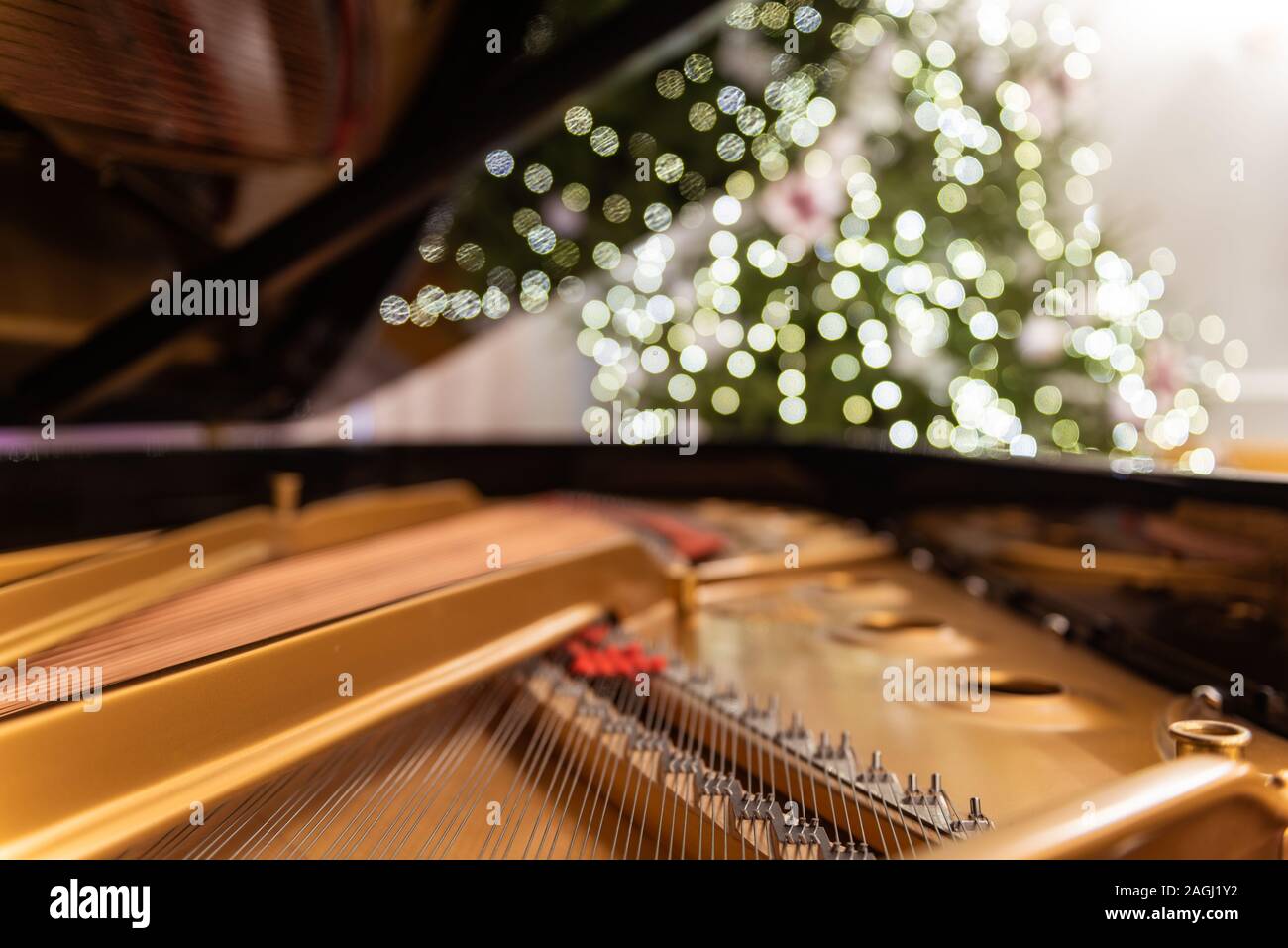 Golden piano Interieur mit sichtbare Zeichenfolgen in den Vordergrund. Im Hintergrund ein unscharfes Weihnachtsbaum mit Ornamenten und Lichtern geschmückt. Stockfoto
