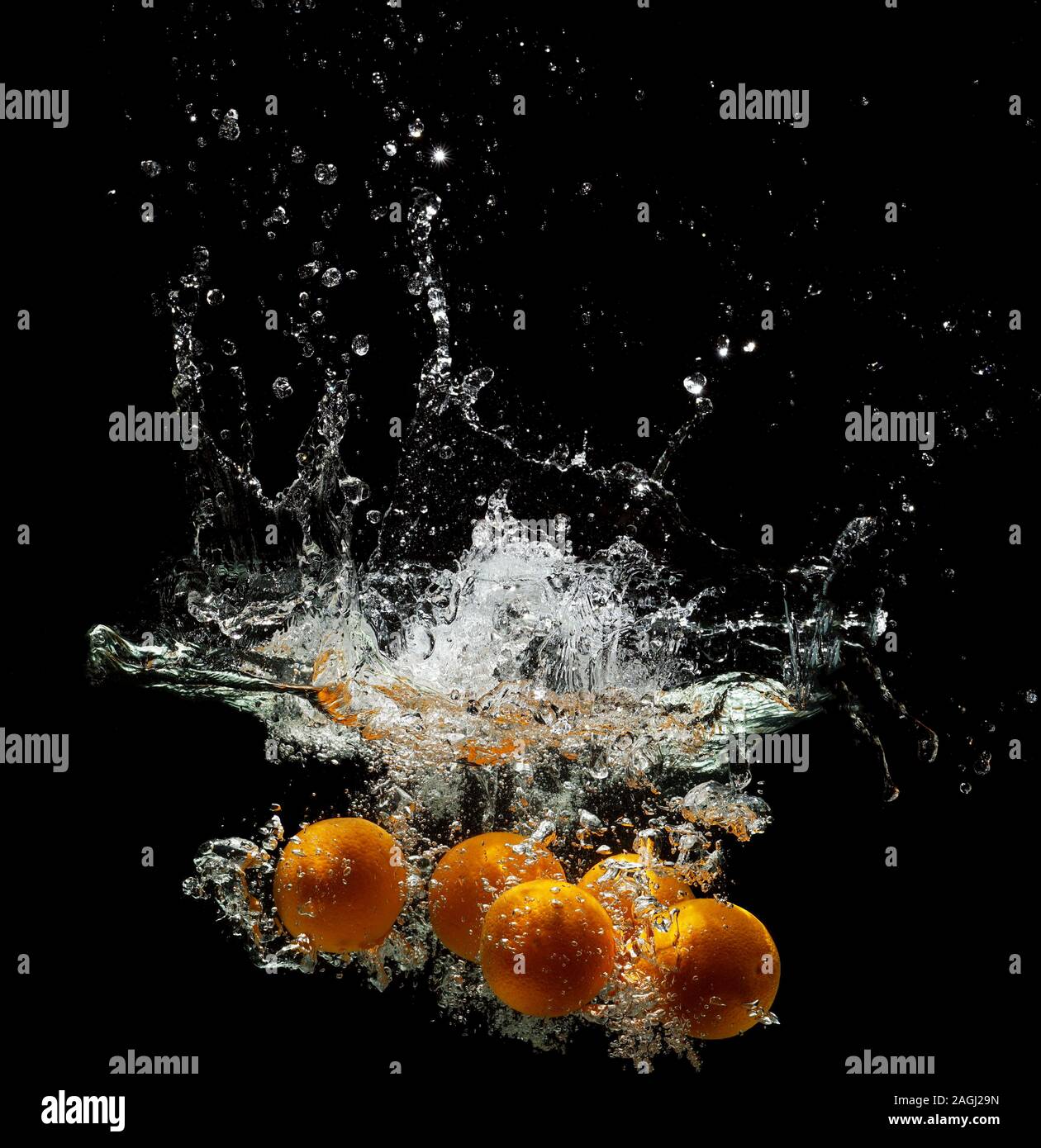 Fünf frische Orangen fallen auf dunklem Grund in Wasser Stockfoto