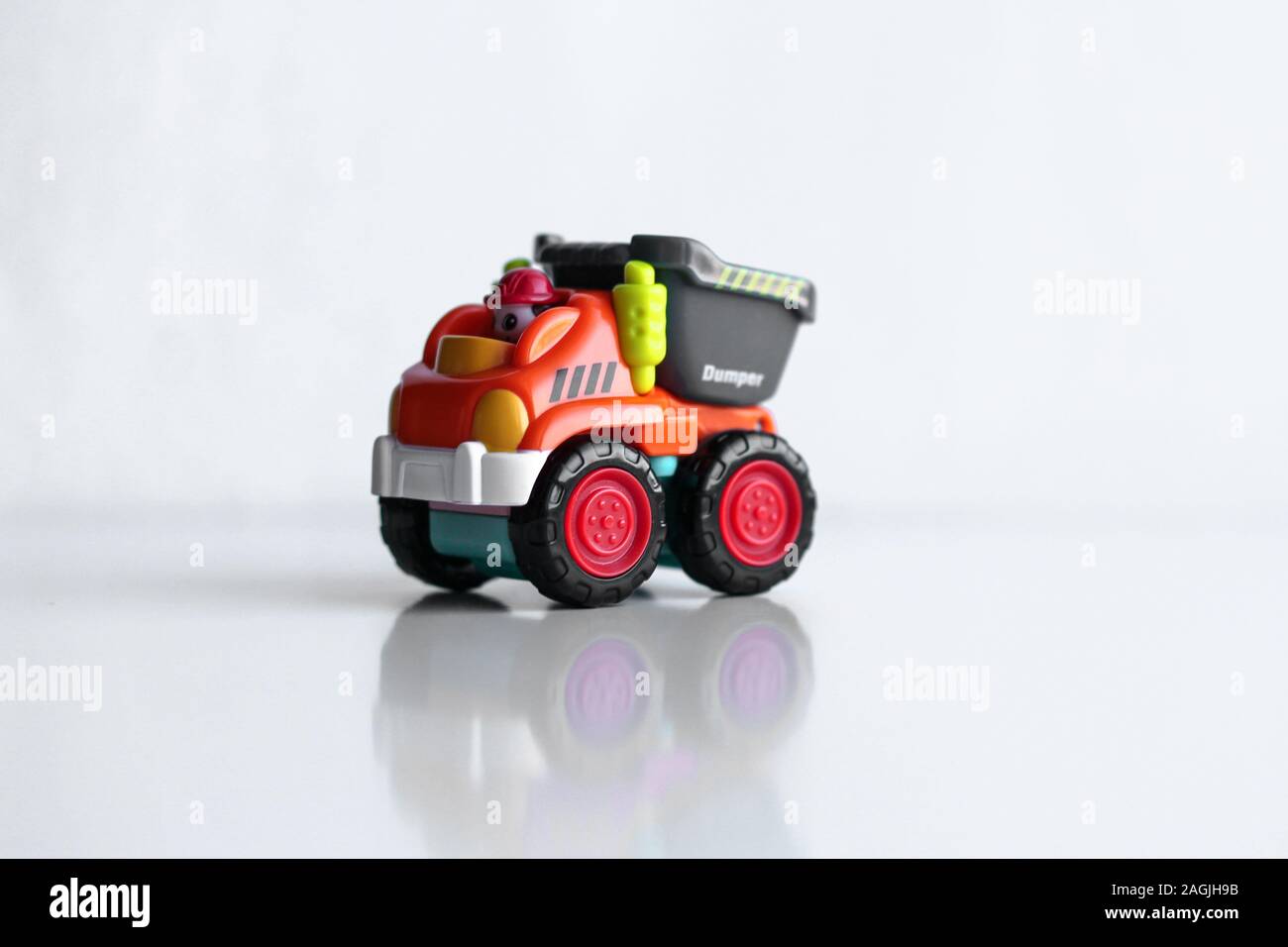 Kunststoff Dump Truck Spielzeug Bau fahrzeug auf weißem Hintergrund mit Reflexion isoliert. Dumper Seite anzeigen. Orange Fahrzeug mit roten Räder und Name Text. Operator in roten Schutzhelm Stockfoto
