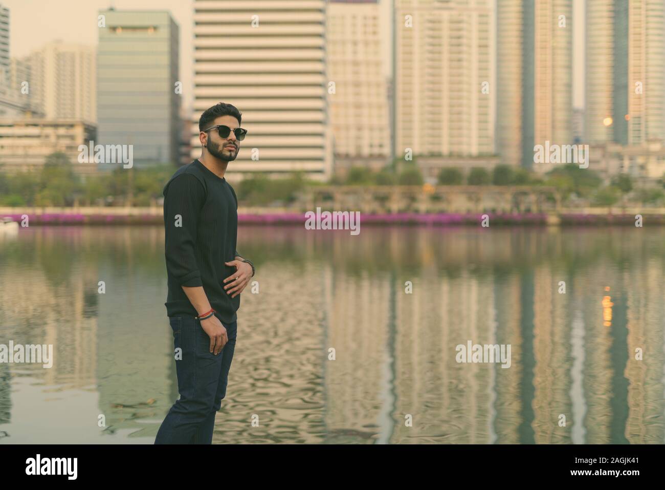 Junge schöne Indische Mann denken, während eine Sonnenbrille gegen den Blick auf den See in der Mitte der Stadt in Bangkok, Thailand Stockfoto