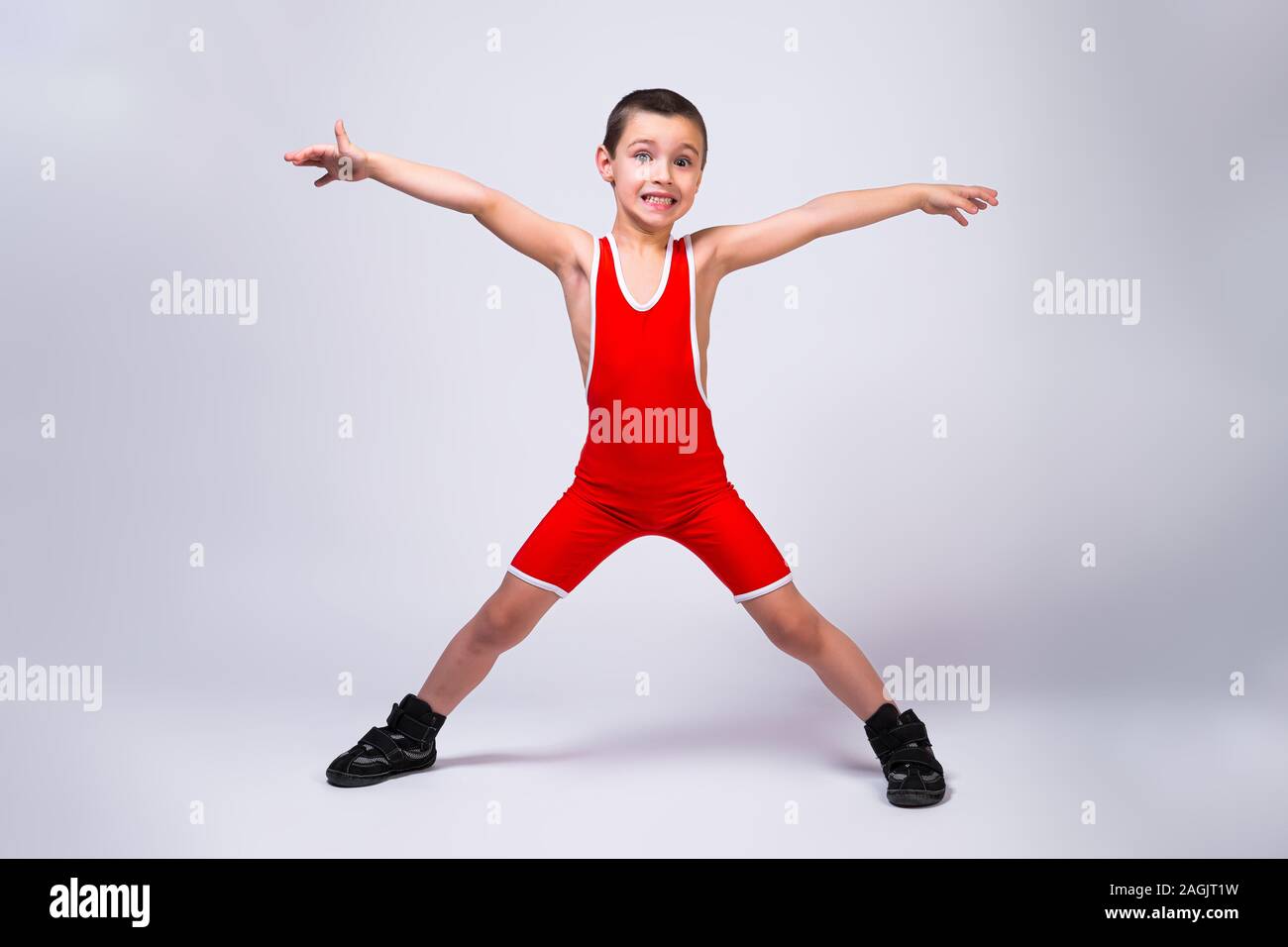 Kleine lustige Junge in einer roten Sport ortsovskoy Turnanzug und wrestling  Stiefel hält, Arme und Beine in verschiedene Richtungen und lächelt seine  Ausführungen auf Stockfotografie - Alamy