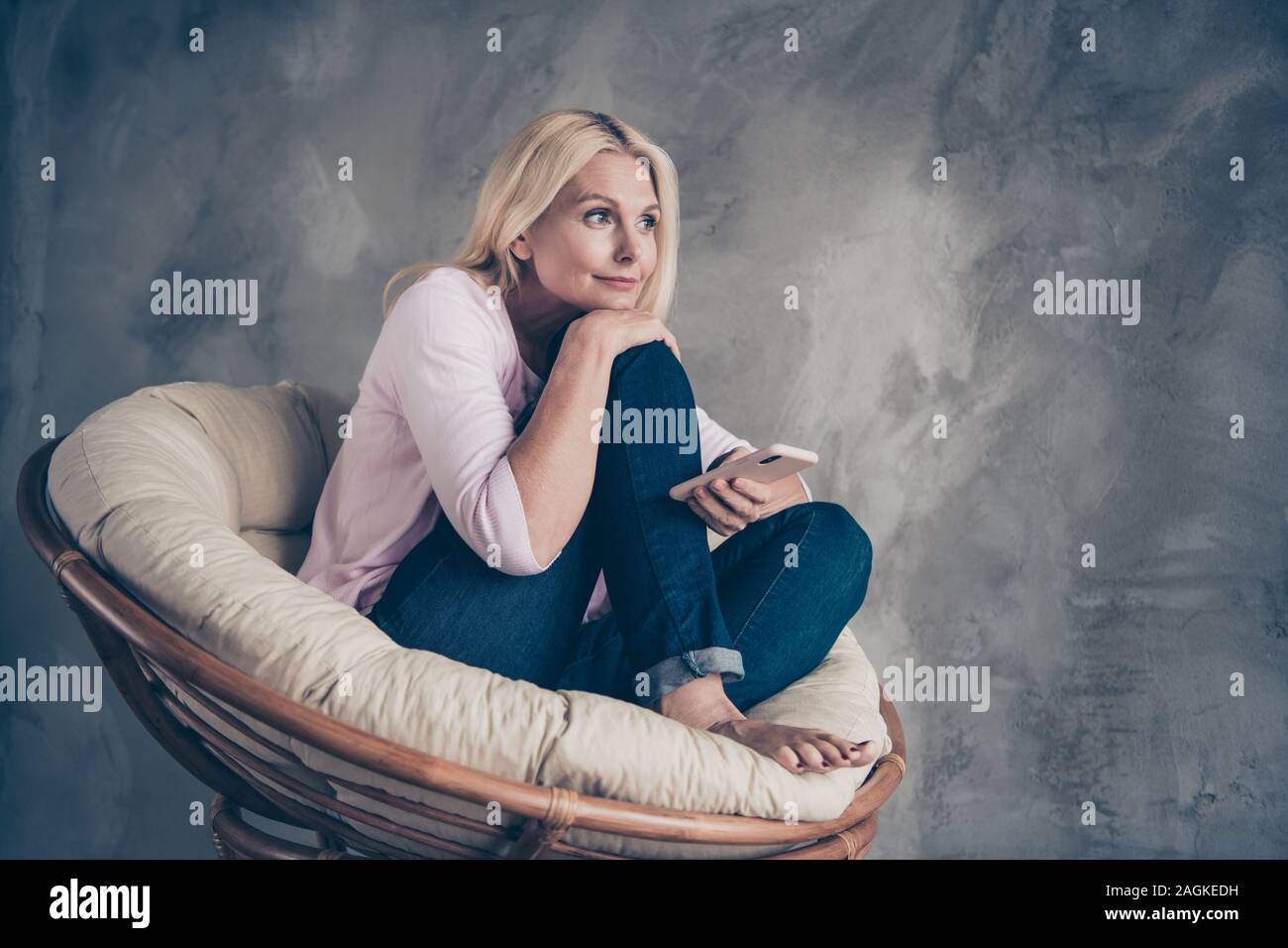 Voller Körper Foto des friedlichen verträumte Frau, die ihr Handy schauen Sie haben Träume Pläne über ihre Wochenenden sitzen in weichen, weißen Sessel im Wohnzimmer Stockfoto