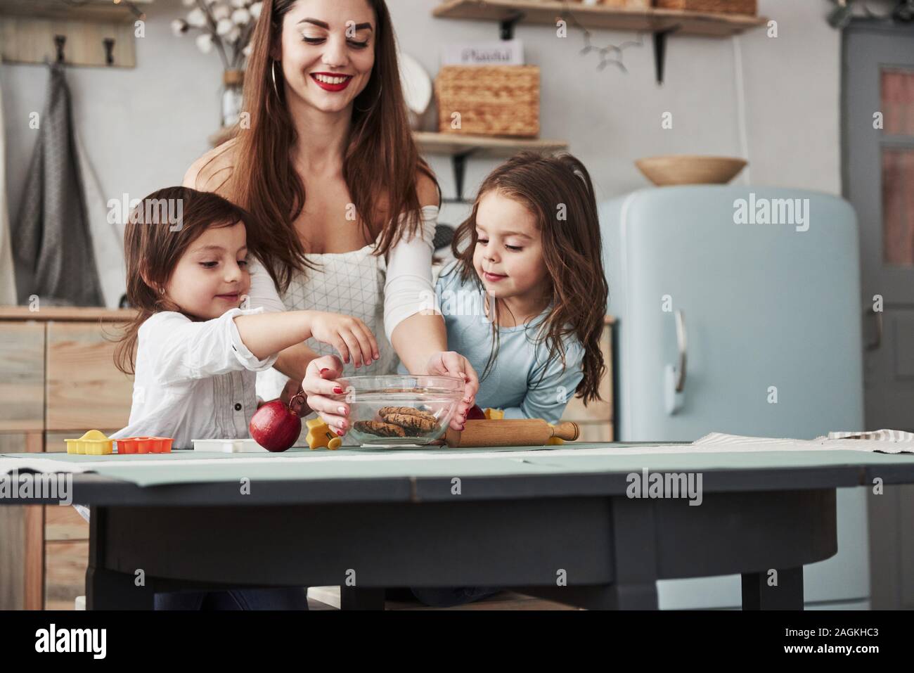 Es ist eine bekannte Tatsache, dass die Kinder Süßigkeiten lieben. Junge schöne Frau geben die Cookies während Sie sitzen in der Nähe des Tisches mit Spielzeug Stockfoto