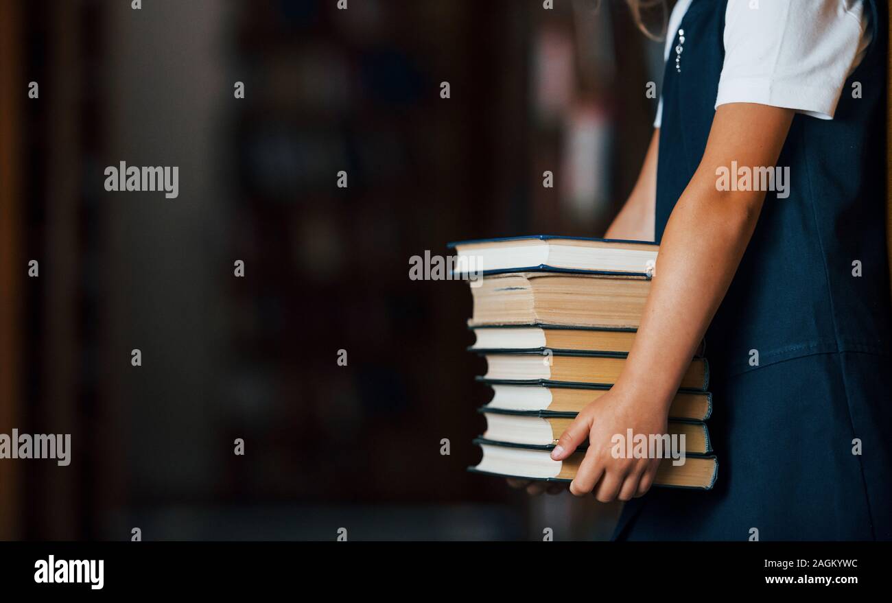 Partikelfilter Blick auf kleine Mädchen hält viele Bücher in die Hände in der Bibliothek Stockfoto