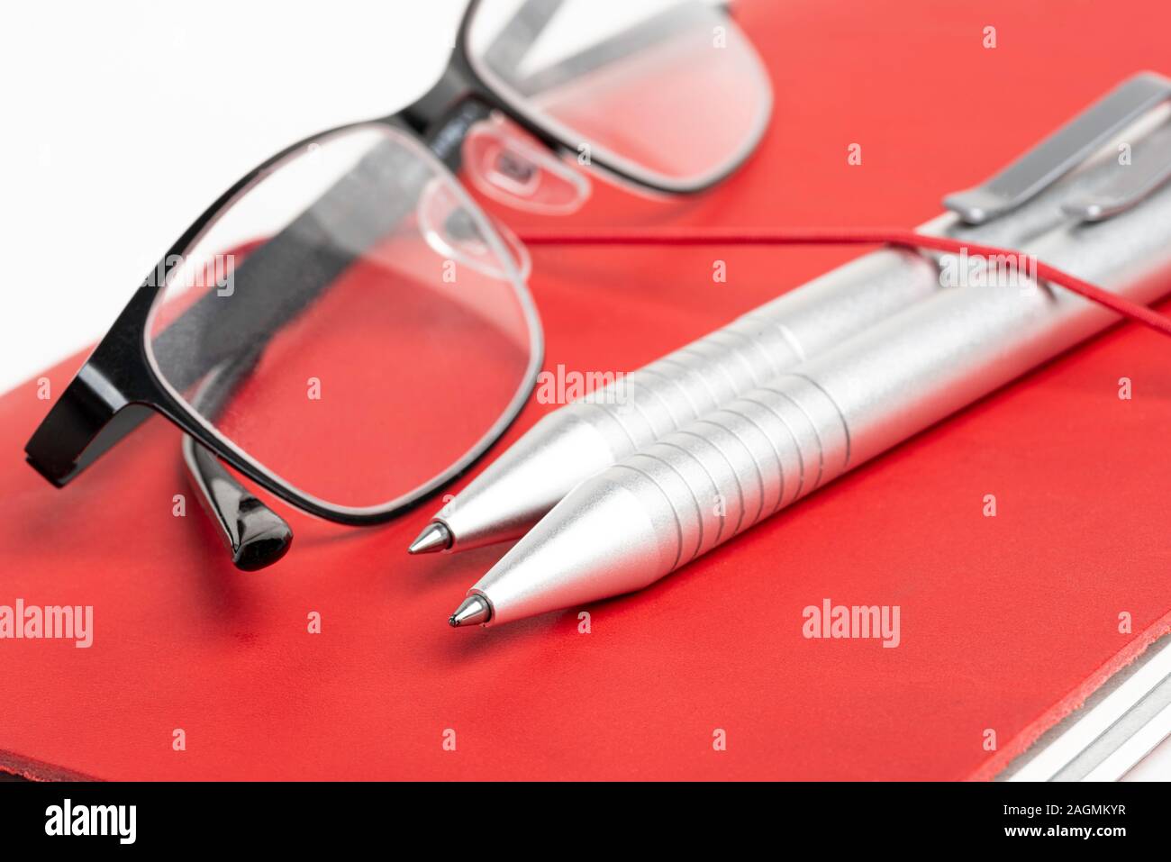Ein Journal mit rotem Leder und elastischem Band, mit zwei silbernen Kugelschreiber und eine Lesebrille. Stockfoto