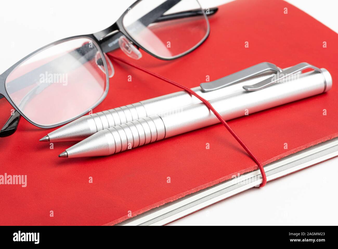 Ein Journal mit rotem Leder und elastischem Band, mit zwei silbernen Kugelschreiber und eine Lesebrille. Stockfoto