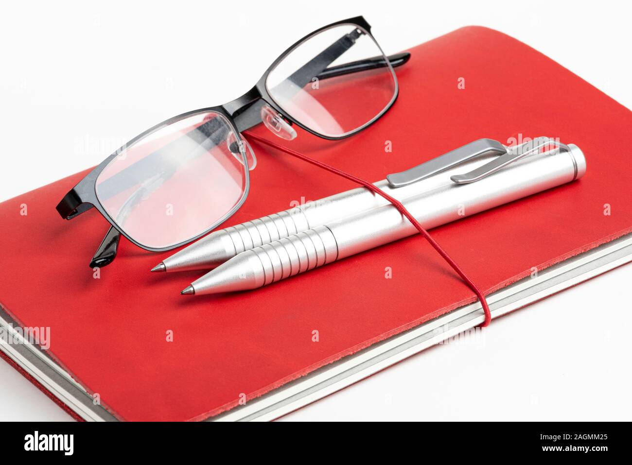 Ein Journal mit rotem Leder und elastischem Band, mit zwei silbernen Kugelschreiber und eine Lesebrille. Stockfoto