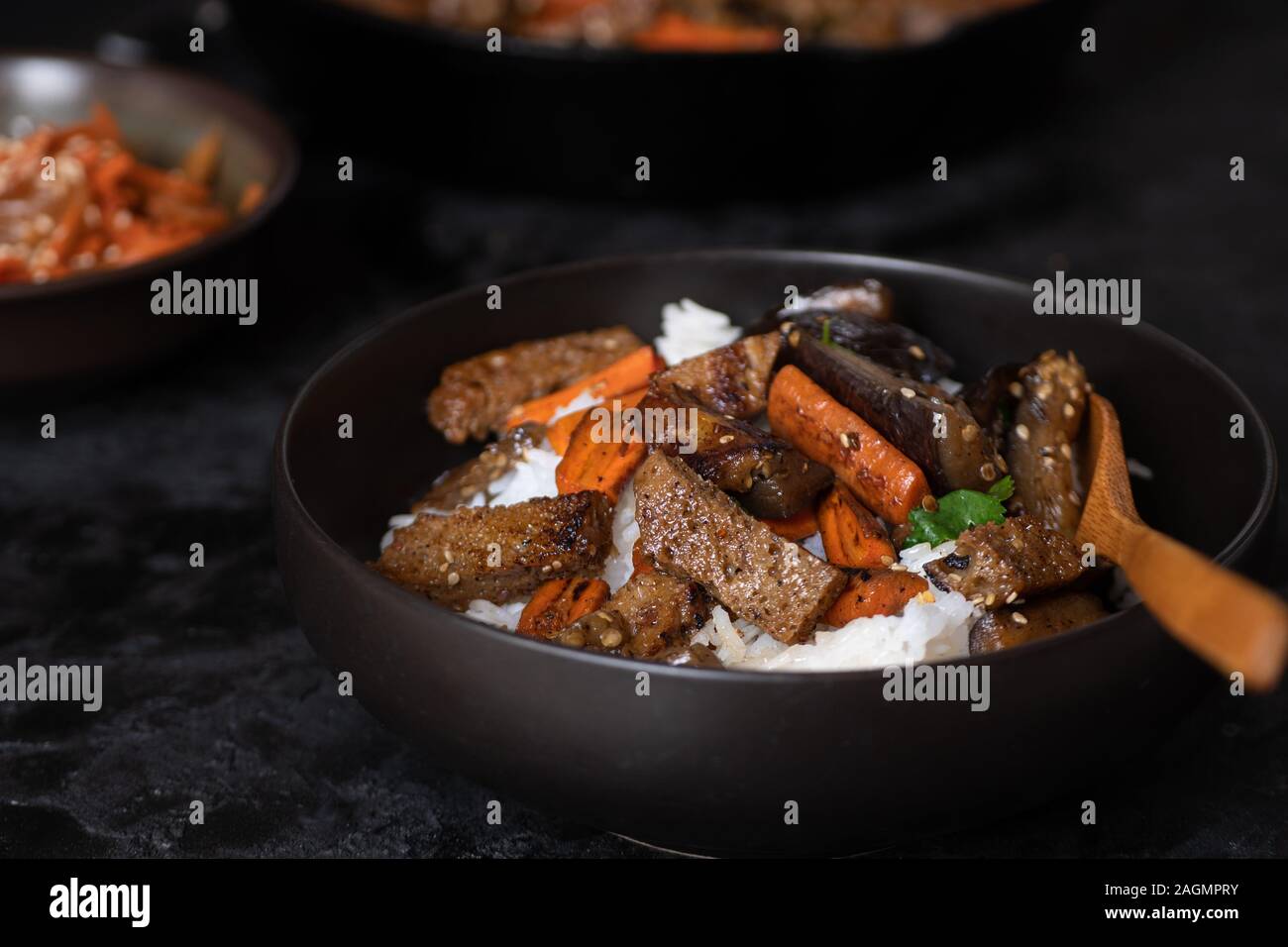 Vegan koreanischen Seitan, Karotte und Auberginen Braten über Reis mit Kimchi in einem schwarzen Schüssel Stockfoto