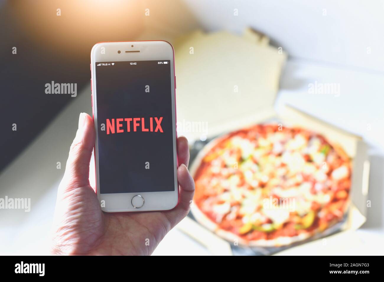 Hand Holding Smartphone mit Netflix Anwendung auf Dem Bildschirm und Pizza im Hintergrund Stockfoto
