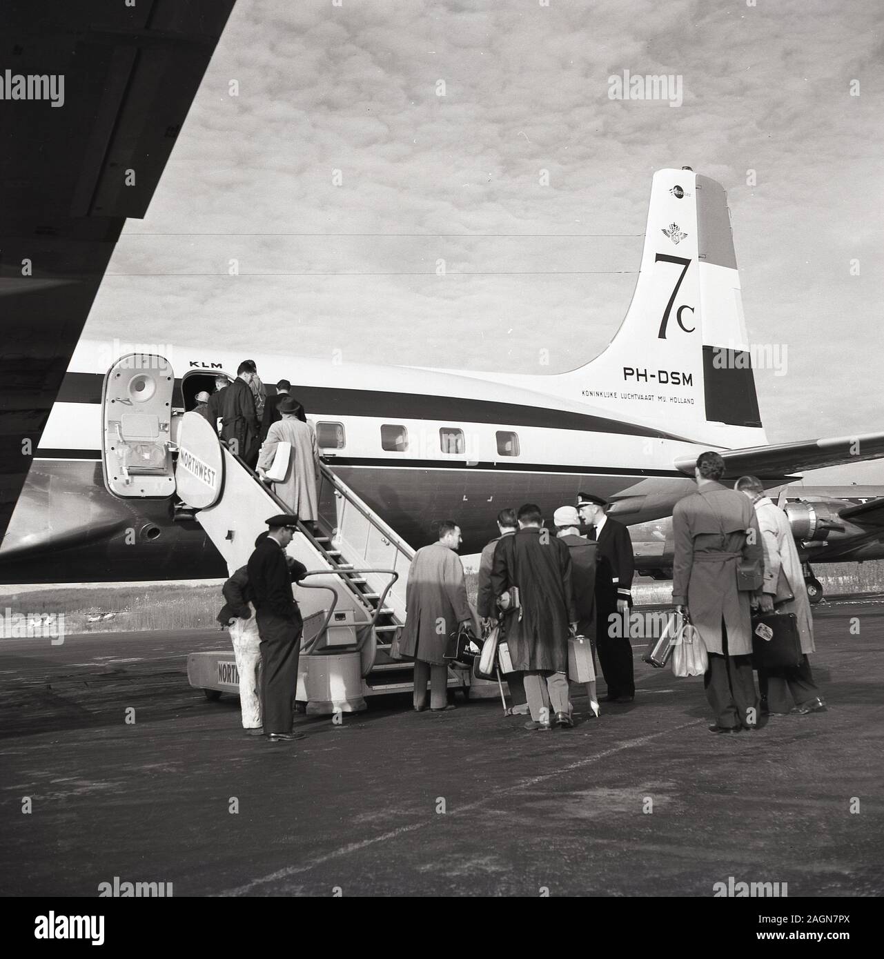 1950s, historische Passagiere, die an Bord eines Dougas DC-7C KLM-Flugzeugs am Flughafen von Anchorage, Alaska, USA, gehen. Die 1956 eingeführte DC-7C (Seven Seas) war eine Variante mit erweiterter Reichweite des ursprünglichen DC-7-Flugzeugs, mit verbesserten Motoren und zusätzlicher Kraftstoffkapazität, was ihr eine durchnon-stop transatlantische Kapazität verleiht und um europäische Fluggesellschaften anzuziehen wurde. Stockfoto