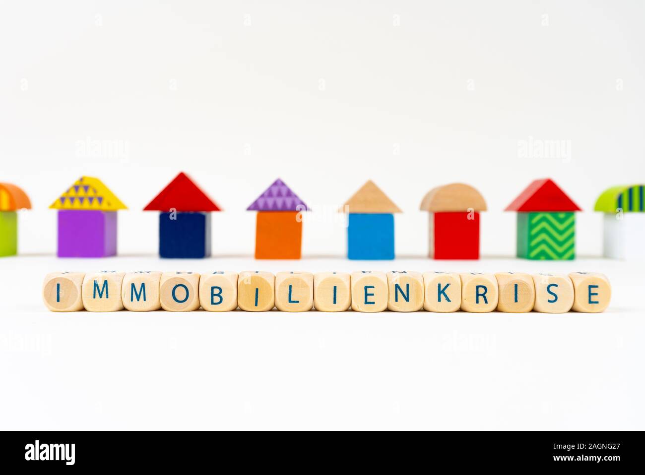 Holzblock mit Buchstaben: "immobilienkrise" (Deutsch für die Immobilienkrise) vor bunten Spielzeug Häuser Stockfoto