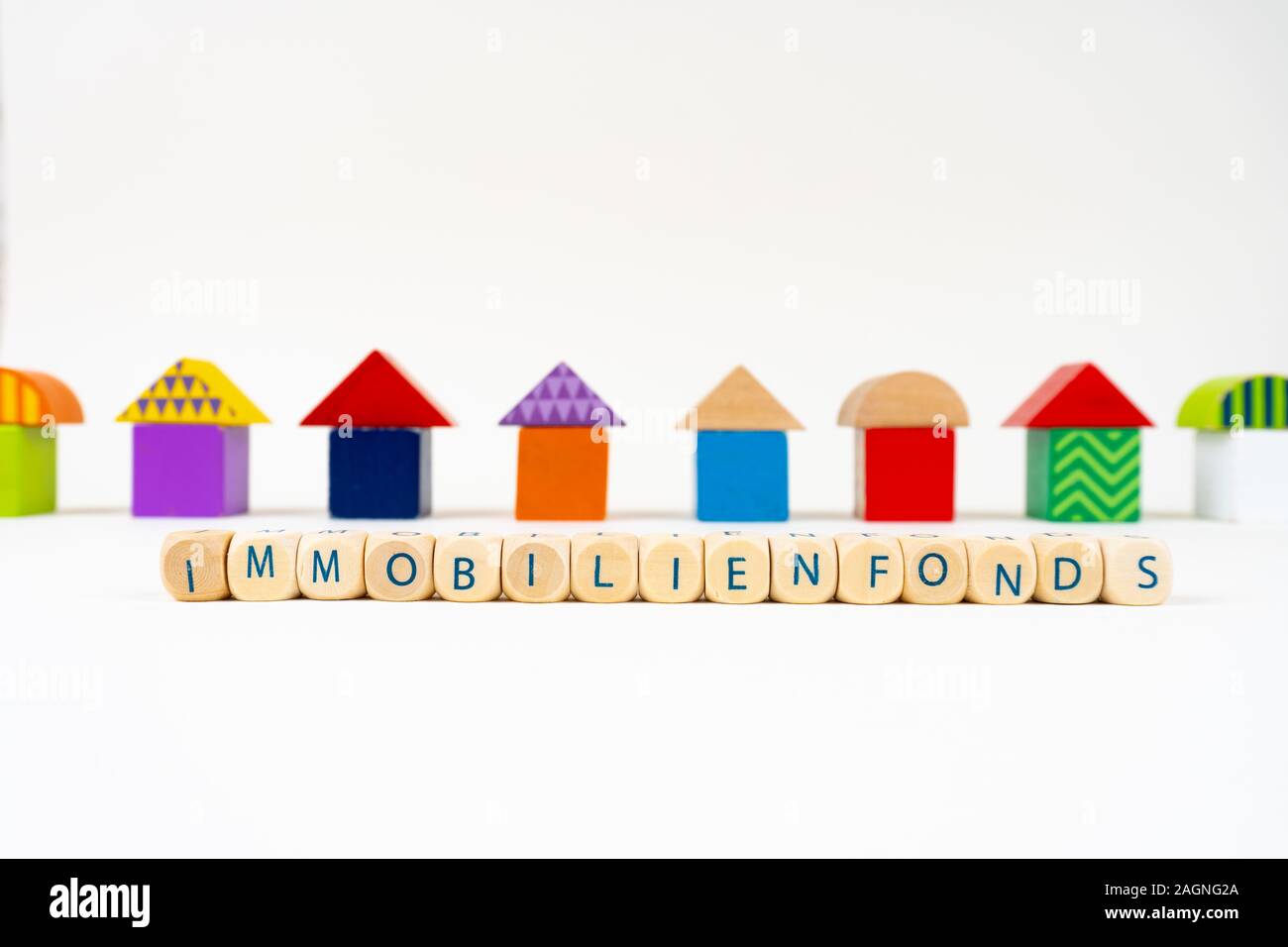 Holzblock mit Buchstaben sagen 'Immobilienfonds' (Deutsch für Immobilienfonds) vor bunten Spielzeug Häuser Stockfoto