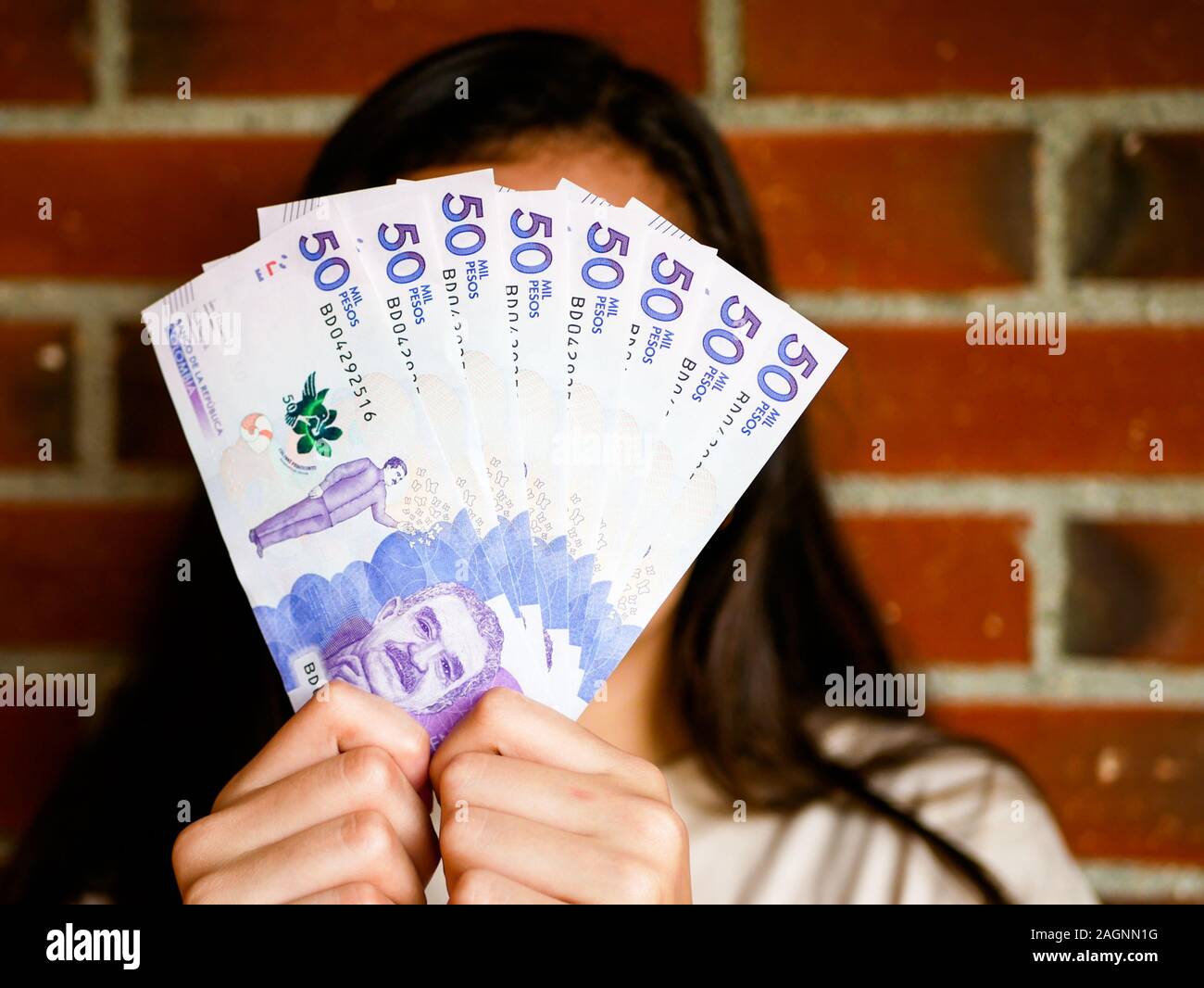 Frau ihr Gesicht verstecken mit einer Reihe von fifthy tousand pesos Bill und Ziegel als Hintergrund Stockfoto