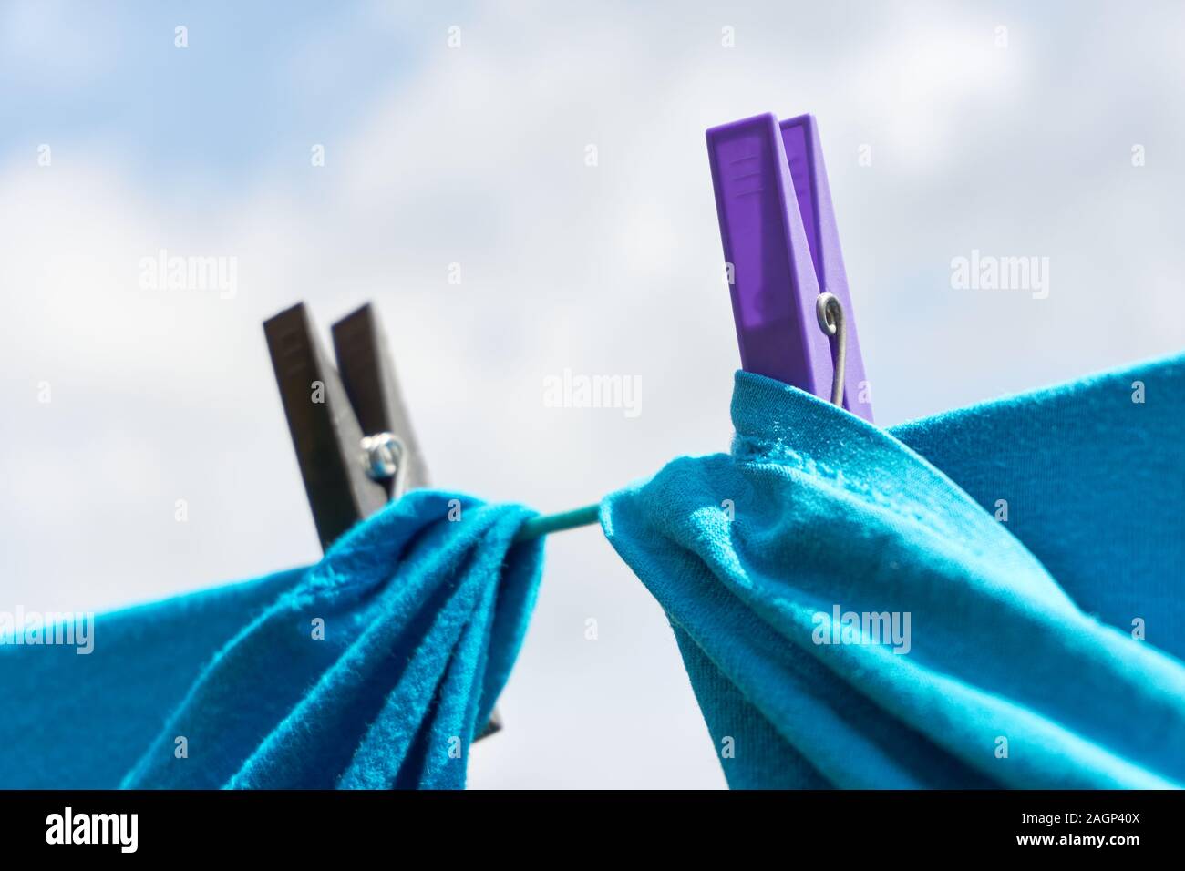 In der Nähe von zwei blauen Shirts trocknen auf eine Wäscheleine mit einem lila und schwarz Wäscheklammer gegen einen bewölkten Himmel Stockfoto