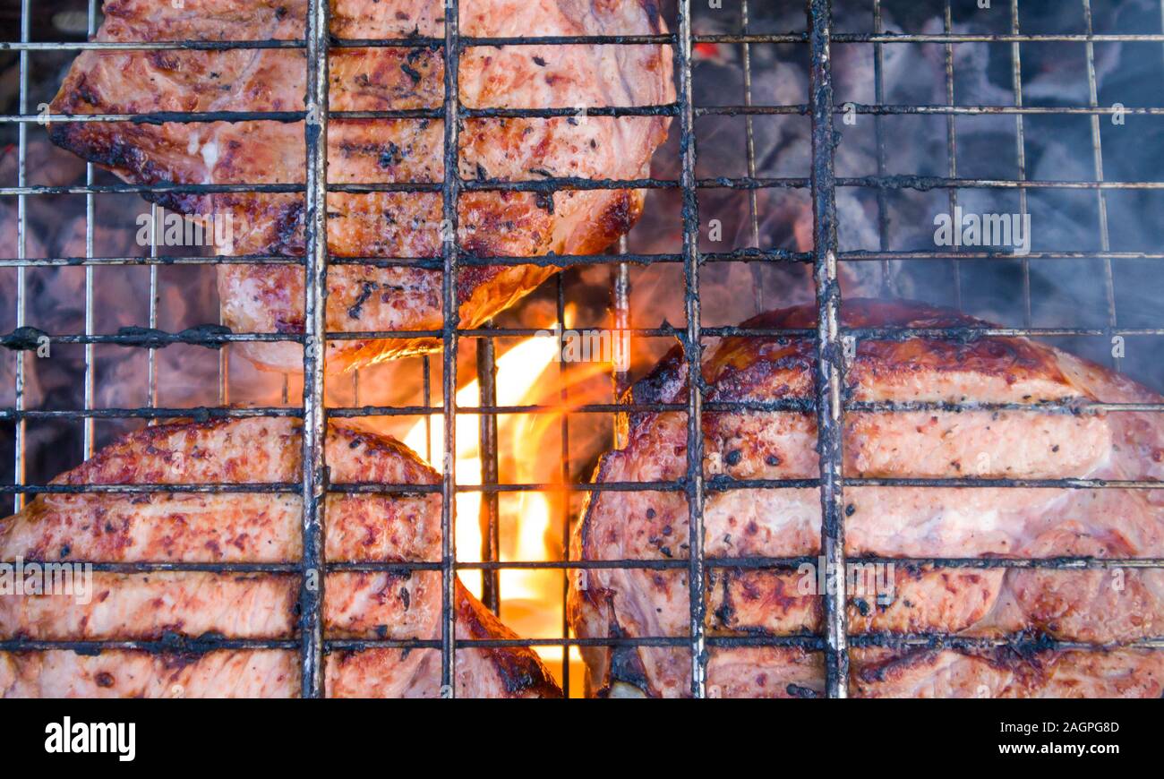 Paar Stücke etwas verbranntem Fleisch auf verkohlte Gitter mit Feuer und Rauch unter Stockfoto