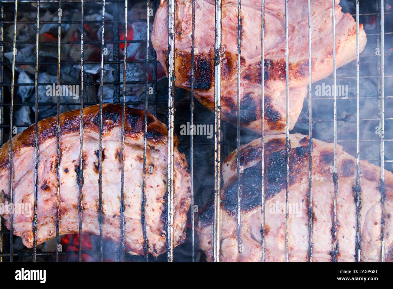 Paar Stücke etwas verbranntem Fleisch auf verkohlte Gitter mit Kohlen und Rauch unter Stockfoto
