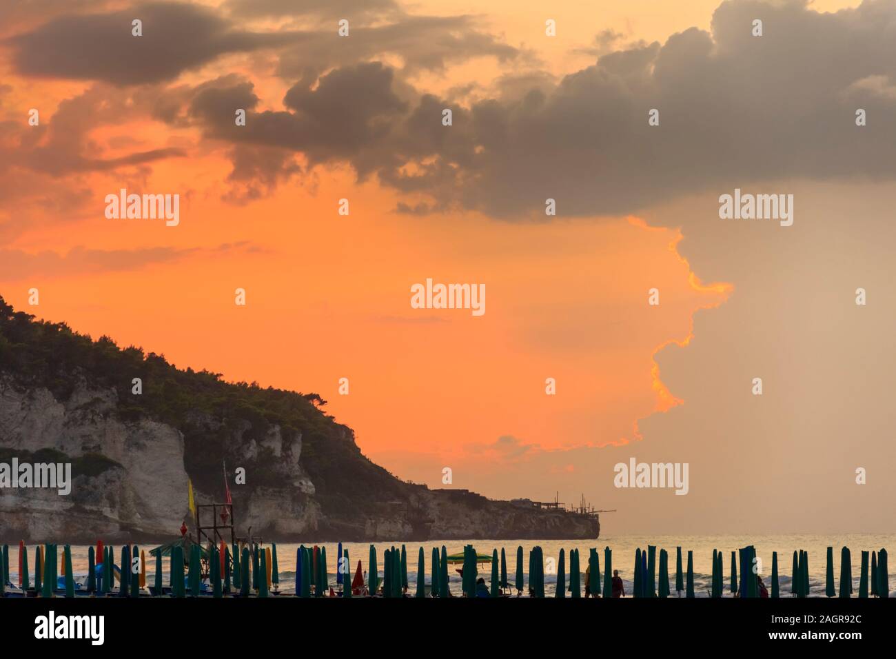 Blick auf die Bucht von Peschici bei Sonnenuntergang: Strand mit Sonnenschirmen, Italien (Apulien). Peschici ist berühmt für seine Badeorte. Stockfoto