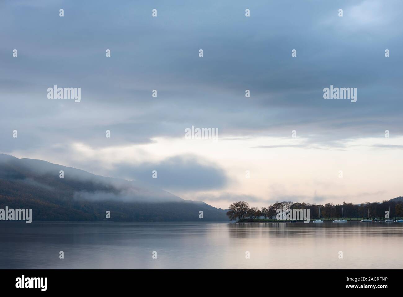 Schönen Sonnenaufgang Landschaft über Coniston Water im Herbst mit Nebel und Wolken wispy Stockfoto