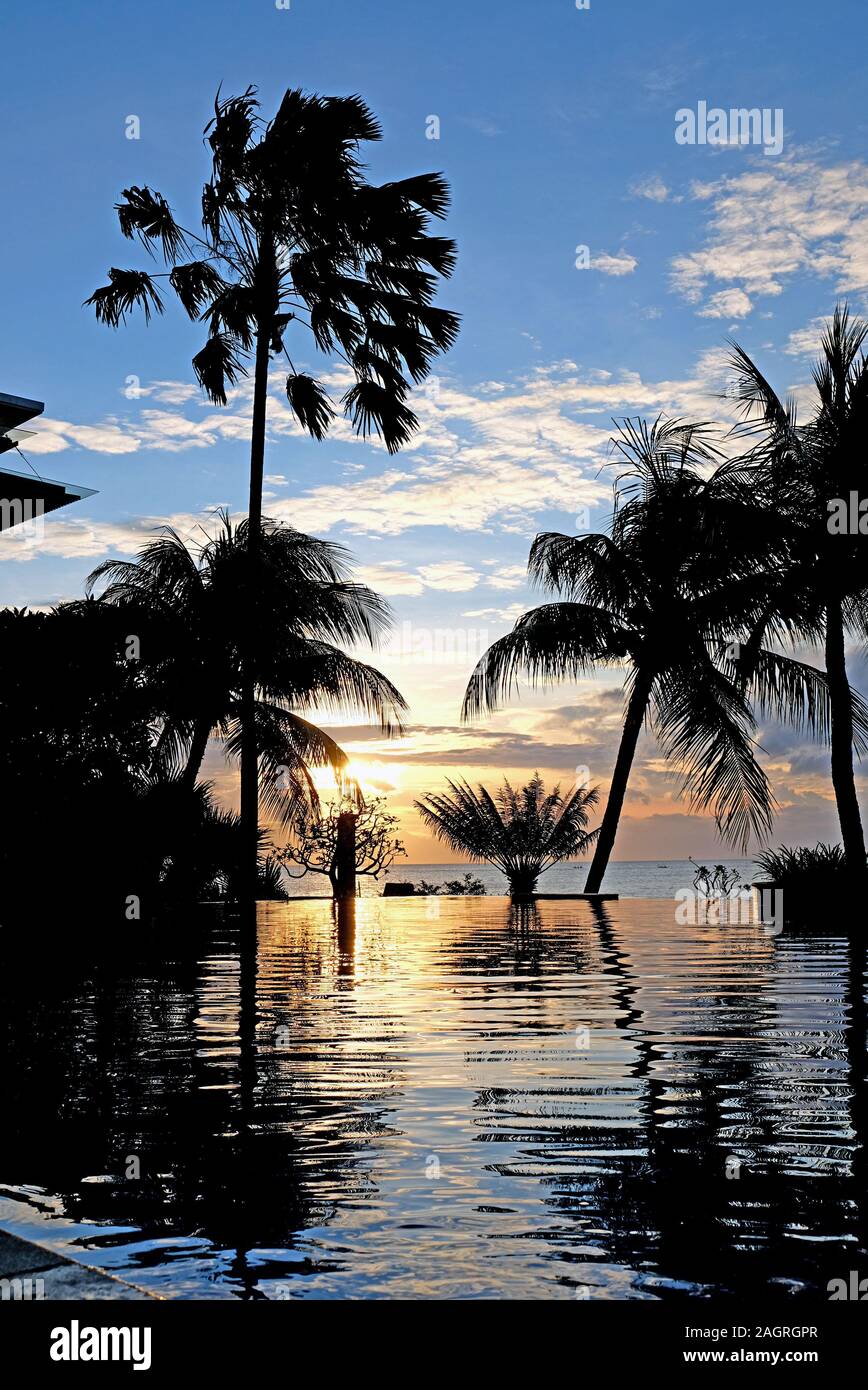 Luxus Pool im Abendlicht mit Sonnenschirmen, Palmen und endlosen Blick auf das Meer. Bali, Indonesien. Stockfoto