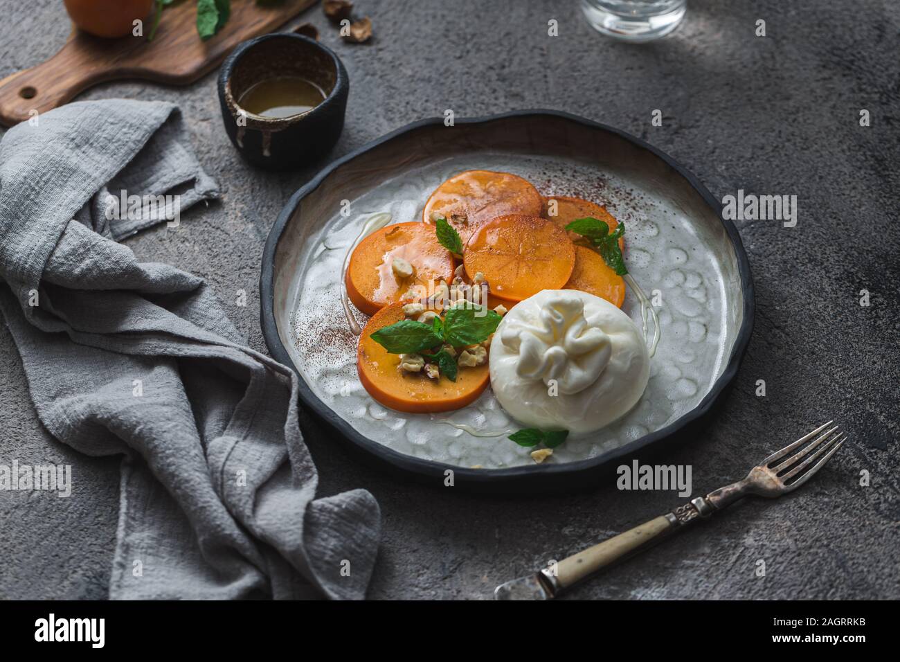 Buratta Käse mit Persimmon auf handgefertigten Teller serviert Stockfoto