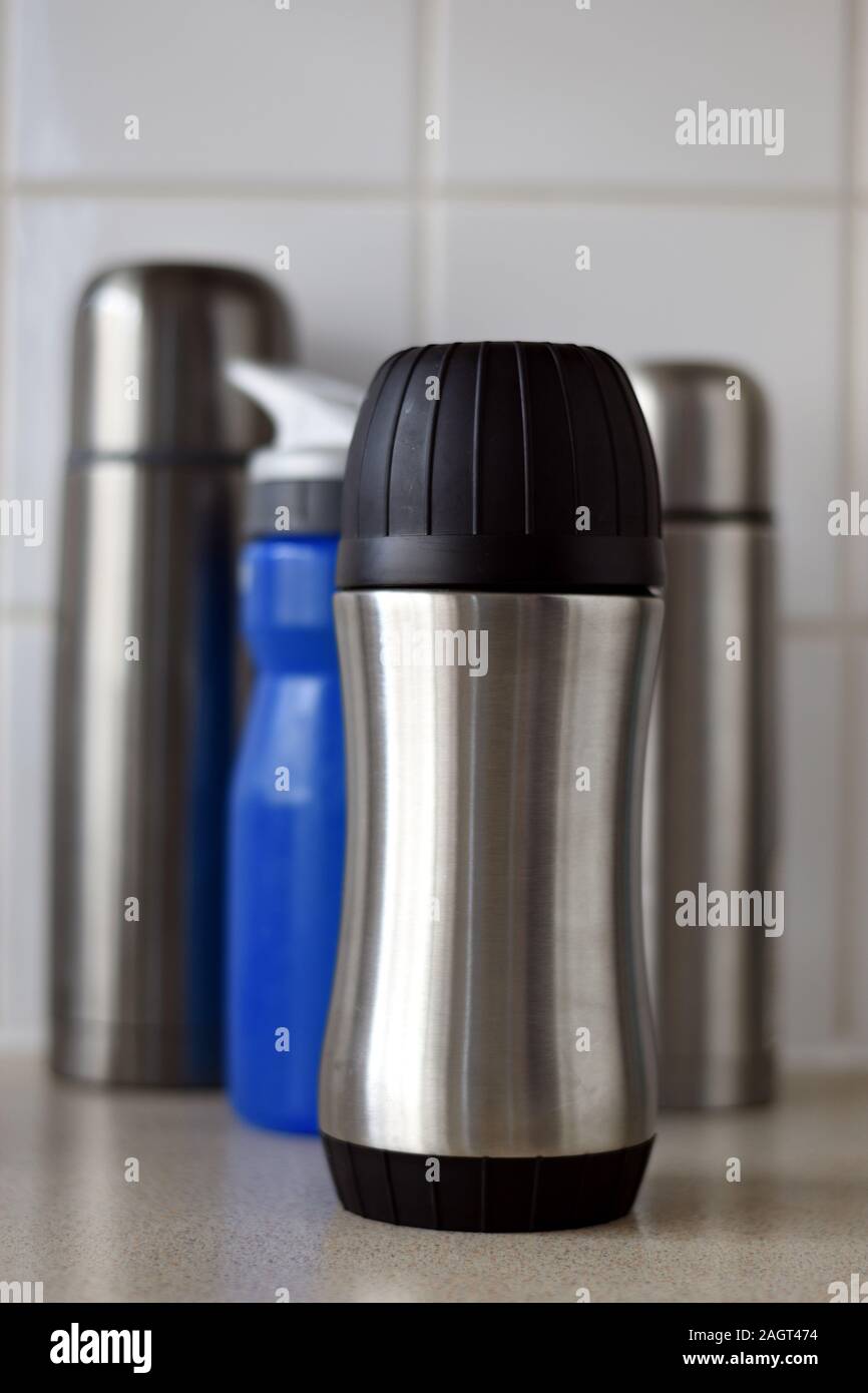 Drei geschlossene Metall heißen Getränk Flaschen. Eine blaue Flasche Wasser. Weiße Fliesen- Hintergrund. Stockfoto