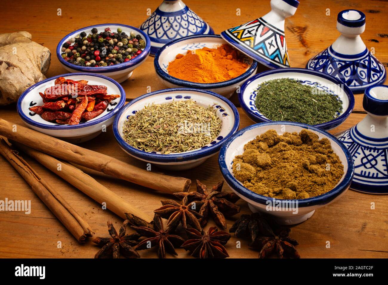 Gesundes Essen. Gewürze in Keramik Behälter typisch für Marokko auf einem alten Holztisch. Farbige Pfeffer, Kurkuma, Cayennepfeffer, Zimt, Ingwer, Kreuzkümmel, Star Stockfoto