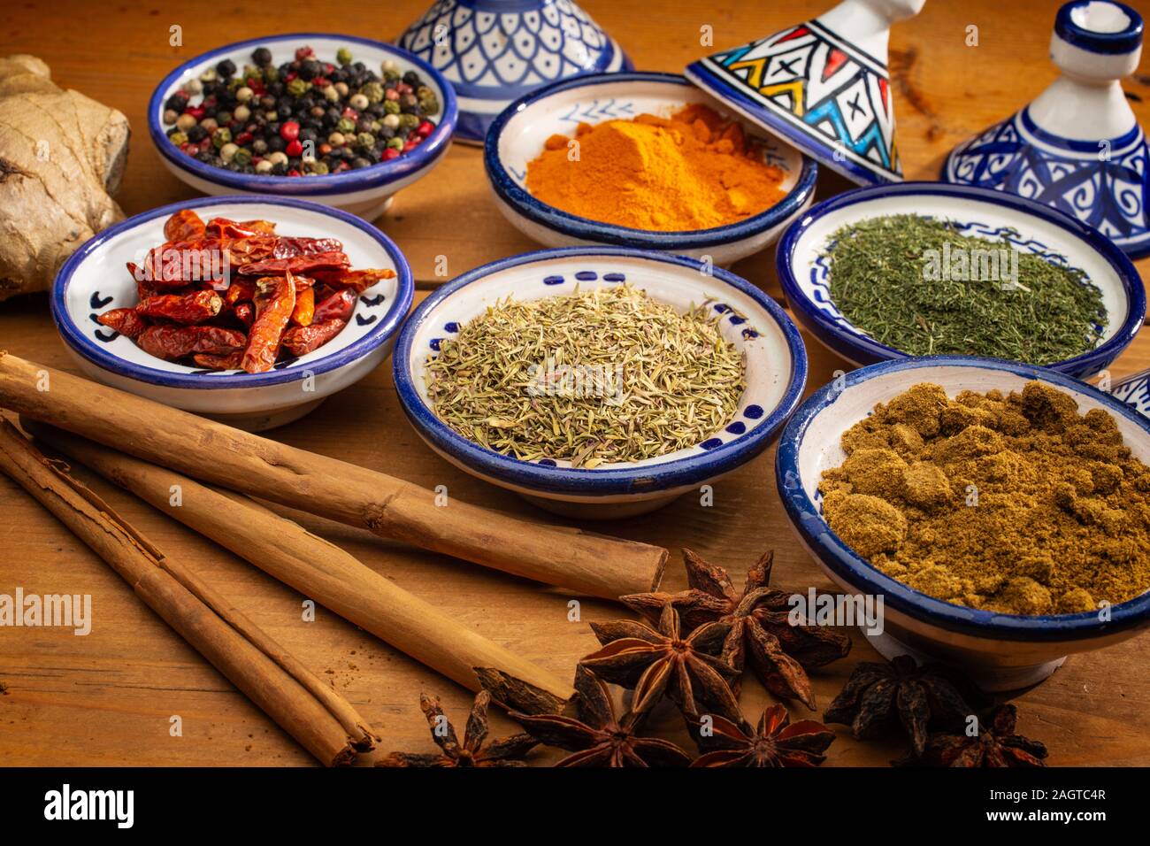 Gesundes Essen. Gewürze in Keramik Behälter typisch für Marokko auf einem alten Holztisch. Farbige Pfeffer, Kurkuma, Cayennepfeffer, Zimt, Ingwer, Kreuzkümmel, Star Stockfoto