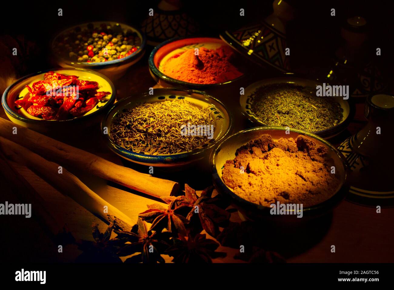 Gesundes Essen. Gewürze in Keramik Behälter typisch für Marokko auf einem alten Holztisch. Farbige Pfeffer, Kurkuma, Cayennepfeffer, Zimt, Ingwer, Kreuzkümmel, Star Stockfoto