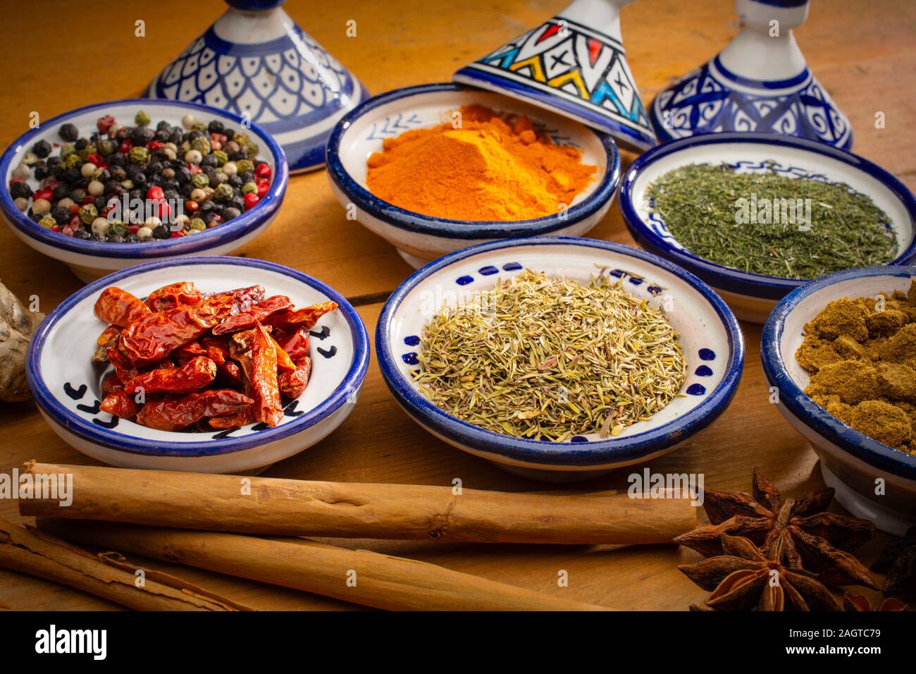 Gesundes Essen. Gewürze in Keramik Behälter typisch für Marokko auf einem alten Holztisch. Farbige Pfeffer, Kurkuma, Cayennepfeffer, Zimt, Ingwer, Kreuzkümmel, Star Stockfoto