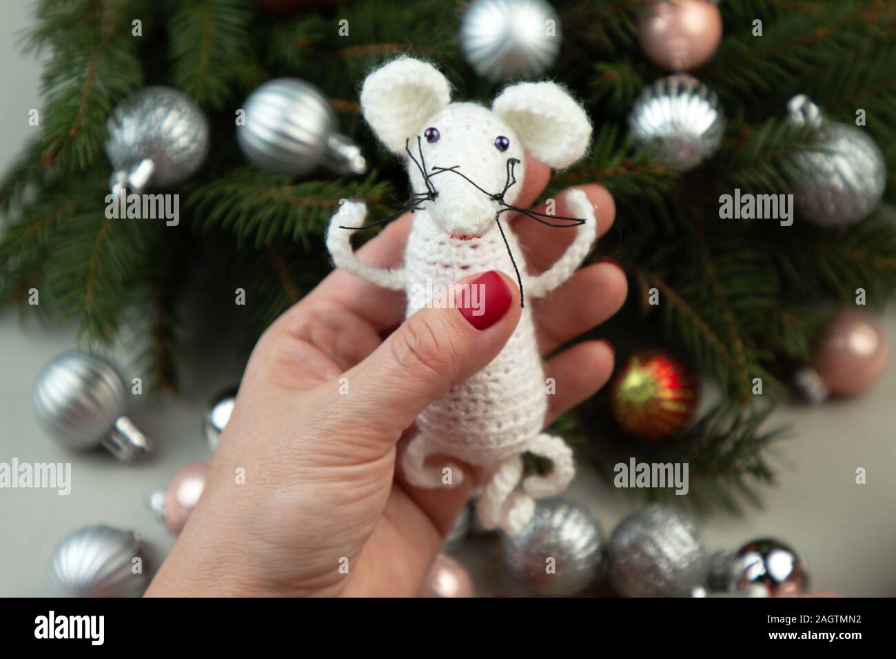 Handarbeit häkeln Spielzeug. Oder weiße Ratte Spielzeug in die Hände auf dem Hintergrund der Weihnachtsbaum. Weihnachten Ratte ist ein Symbol für das neue Jahr 2020. Stockfoto