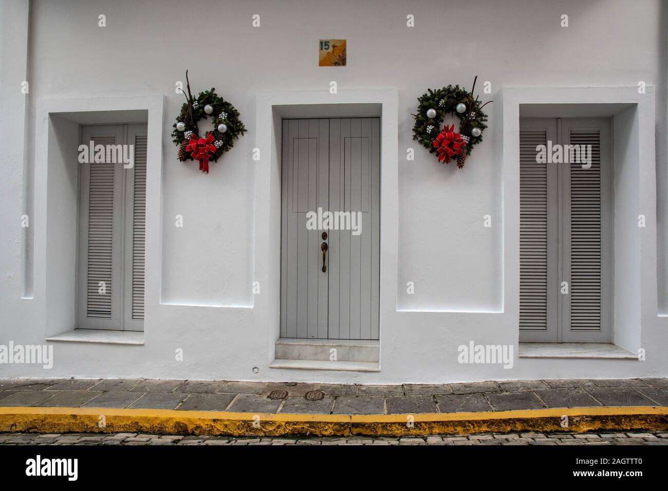 Diese Tür und der 2 Fenster sind Teil eines Stadthauses, weißes Gebäude in der historischen Altstadt San Juan gemalt. Die weißen Wände sind mit 2 Kränzen dekoriert. Stockfoto