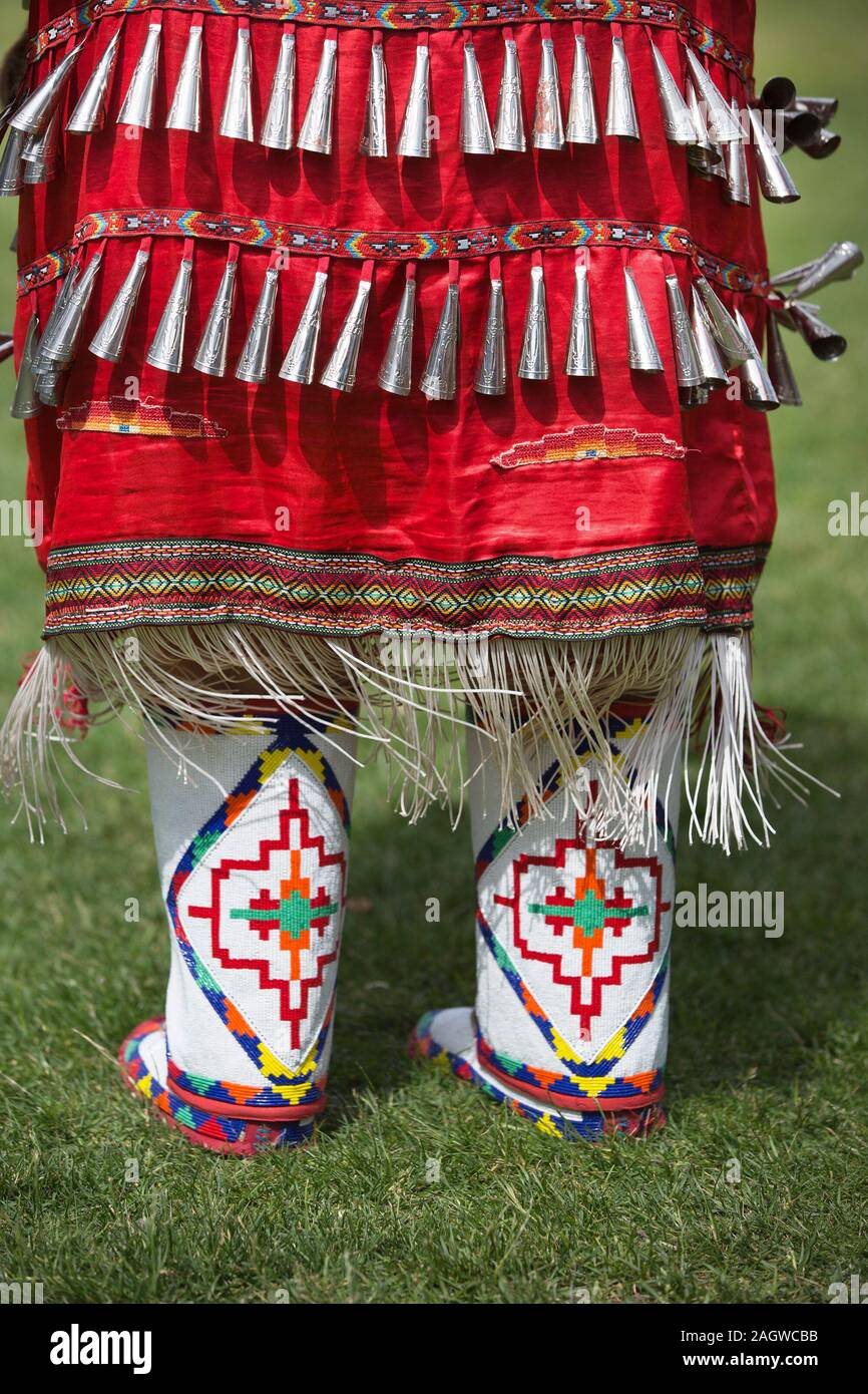 Details aus nächster Nähe zu roten Klingeltanzkostümen und Mokassinen, die von einer einheimischen Frau im Canada Day Powwow getragen wurden. Stockfoto