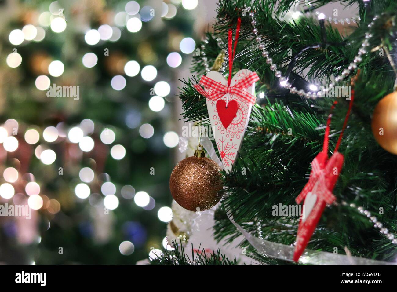 Geschmückten Weihnachtsbaum zu Hause mit roten Herzen Spielzeug und Lichter und Bokeh verschwimmt defokussierten Reflexion Hintergrund Platz für Text. Merry Xmas und Happ Stockfoto