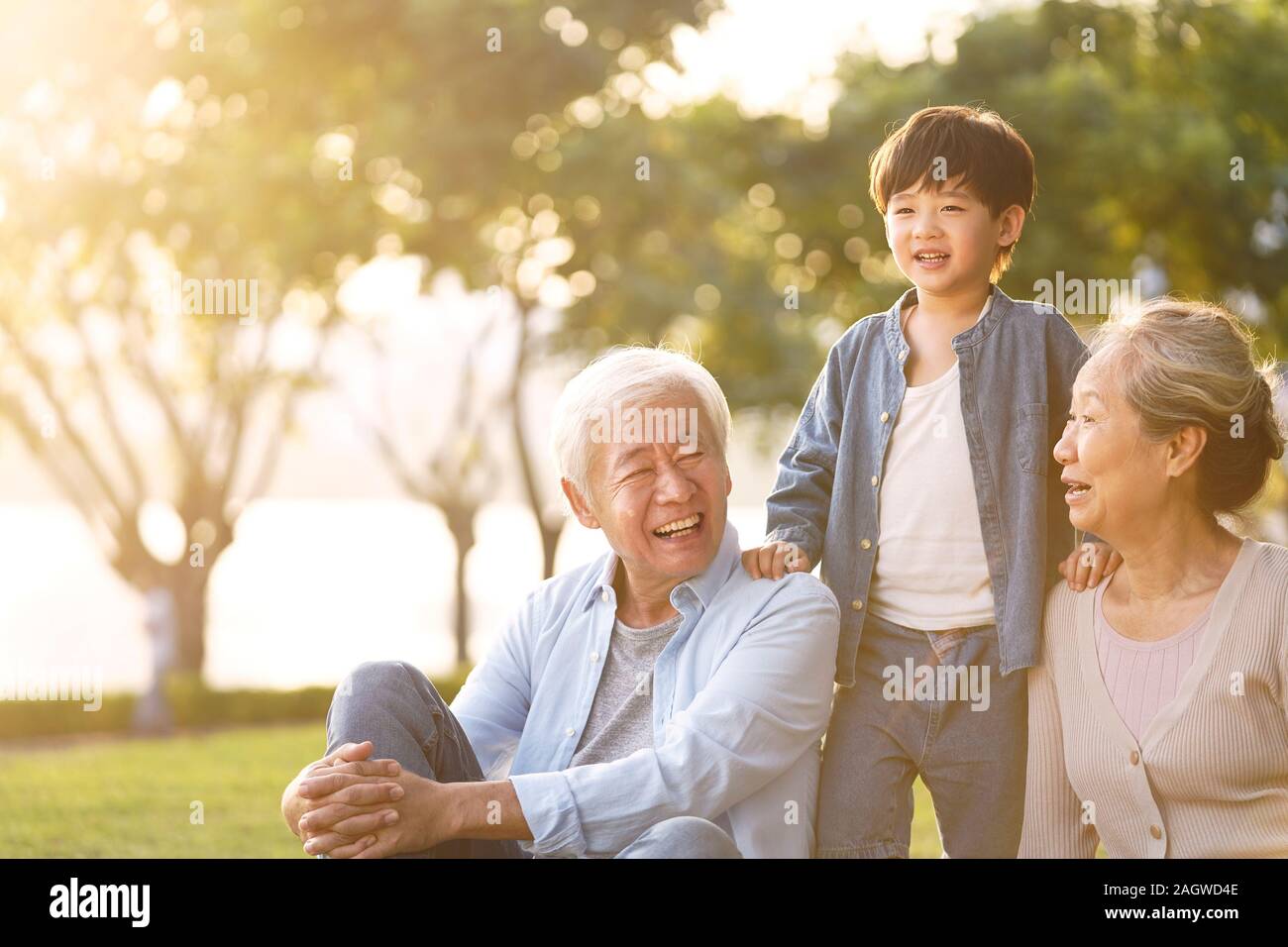 Asiatische Enkel, Großvater und Großmutter saß plaudernd auf Gras draußen im Park in der Dämmerung Stockfoto