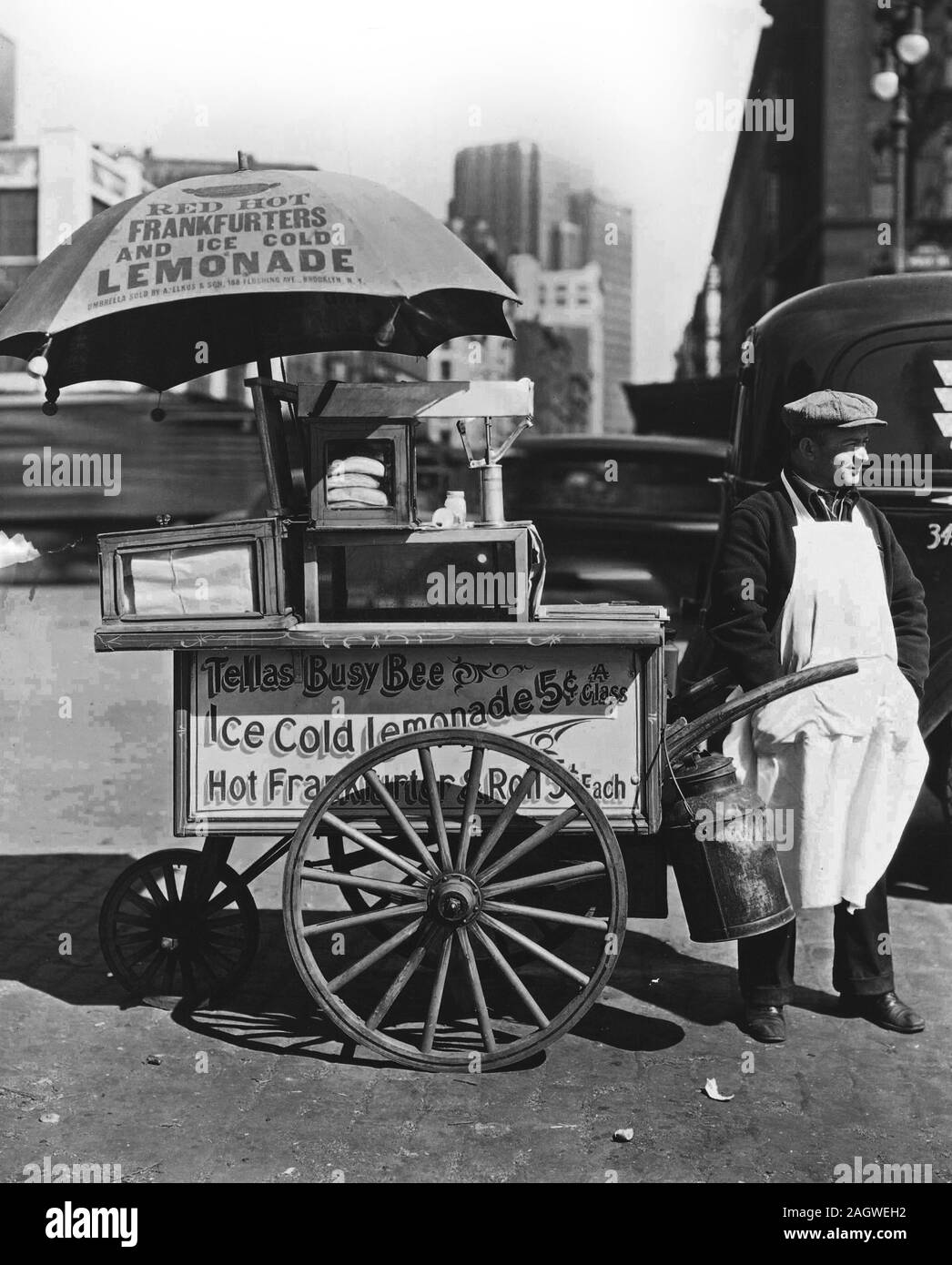 1930 New York City - Hot Dog Stand, die West St. und North Moore. Anbieter steht neben seinem Tellas Busy Bee Warenkorb, Werbung "Rote heiße Würstchen und eiskalte Limonade ' Verkehr eine Unschärfe im Hintergrund. 1936 Stockfoto