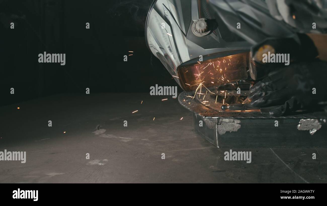 Schmiedewerkstatt. Schmiede. Arbeiter in einer Schweißen Haube Helm Schweißnähte ein Teil von elektrischem Schweißen. Funken sind in den Schutzschirm wider. Stockfoto