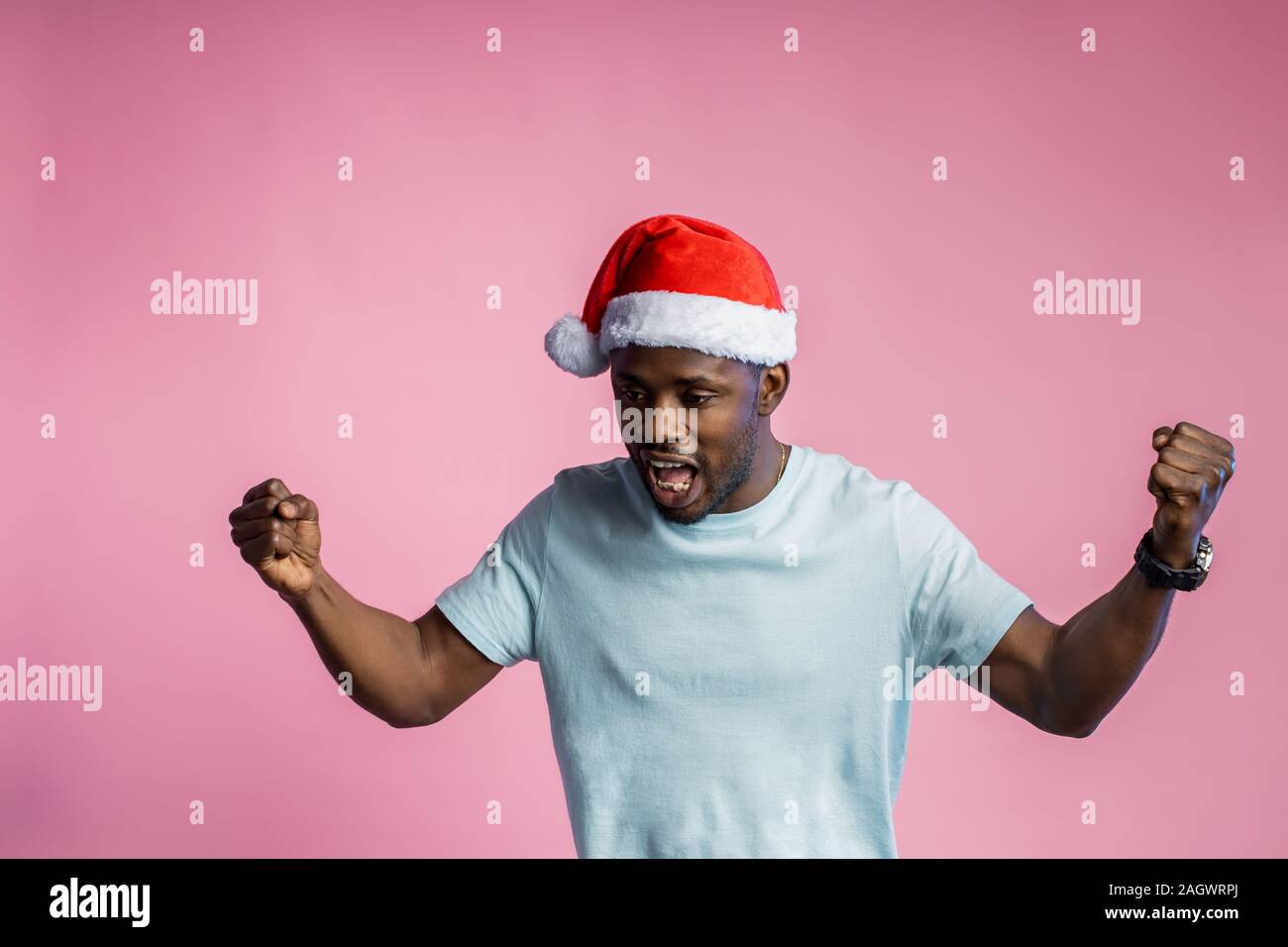 Wütend, wütend afrikanischer Mann ballte die Fäuste und Zähne, Hände, tragen t-shirt, Santa Hut, Pläne für Weihnachten nicht wahr, auf Rosa posing b Stockfoto