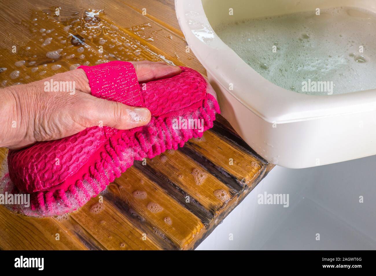 Nahaufnahmen eines Menschen Hand Waschen einer Kiefer spüle Arbeitsplatte/Zähler mit einem rosa Schwamm. Ein plastik Schüssel voller Seifenlauge ist neben. Stockfoto