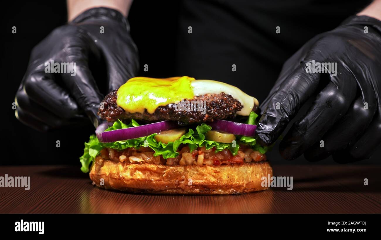 Handwerk Burger ist Kochen auf schwarzem Hintergrund. Bestehen: salsa Sauce, Salat, rote Zwiebel, Gurke, Käse, Chili, Paprika, Brötchen, marmoriertes Fleisch Rindfleisch. Stockfoto