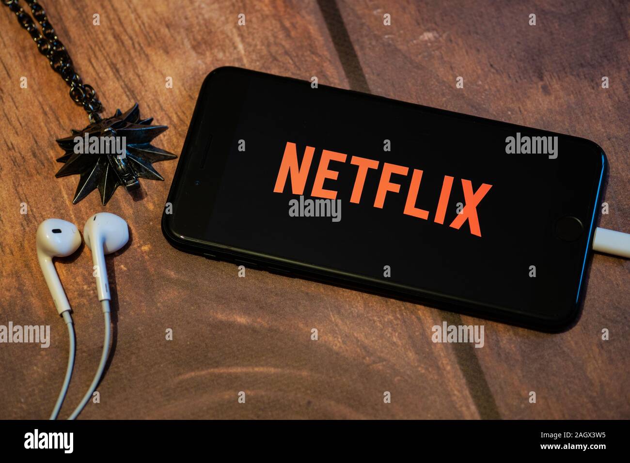 NIZHYN, UKRAINE / 21 Dezember 2019: Kopfhörer, der Witcher Medaillon und iPhone mit Logo von Netflix auf dem Bildschirm. TV-Serie "The Witcher" Premiere Stockfoto