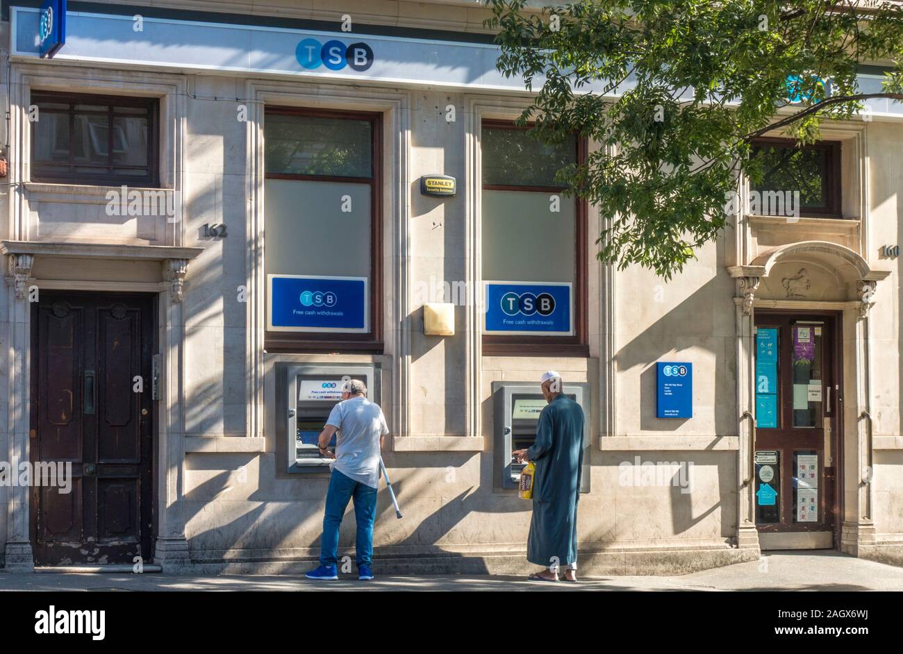 Zwei Männer machen Bargeldabhebungen an Geldautomaten außerhalb einer Niederlassung der TSB Bank auf einer sonnigen und ruhigen Morgen. High Street, Acton, London, W3, England, UK. Stockfoto