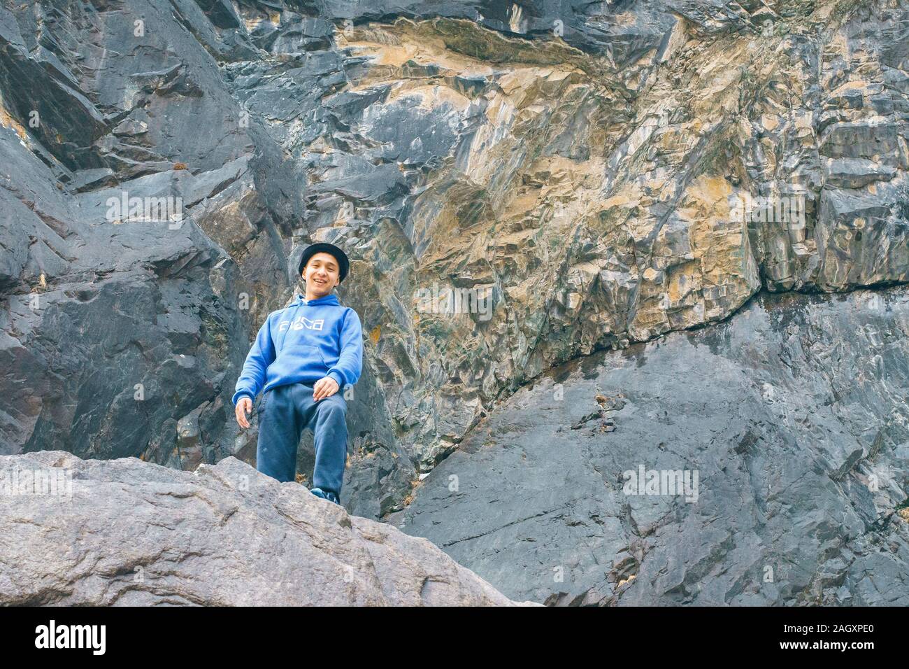 Belogorka, Kirgisistan - März 25, 2018: Yong Mann in einer blauen Jacke in den Bergen zwischen Felsen. Gelb Schwarz Berg Stockfoto