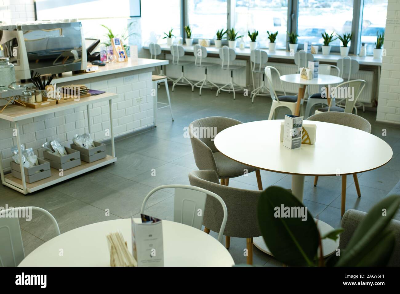 Weiße, runde Tische mit bequemen Sesseln und Stühlen entlang Fenster im Innern gemütliches Cafe umgeben Stockfoto