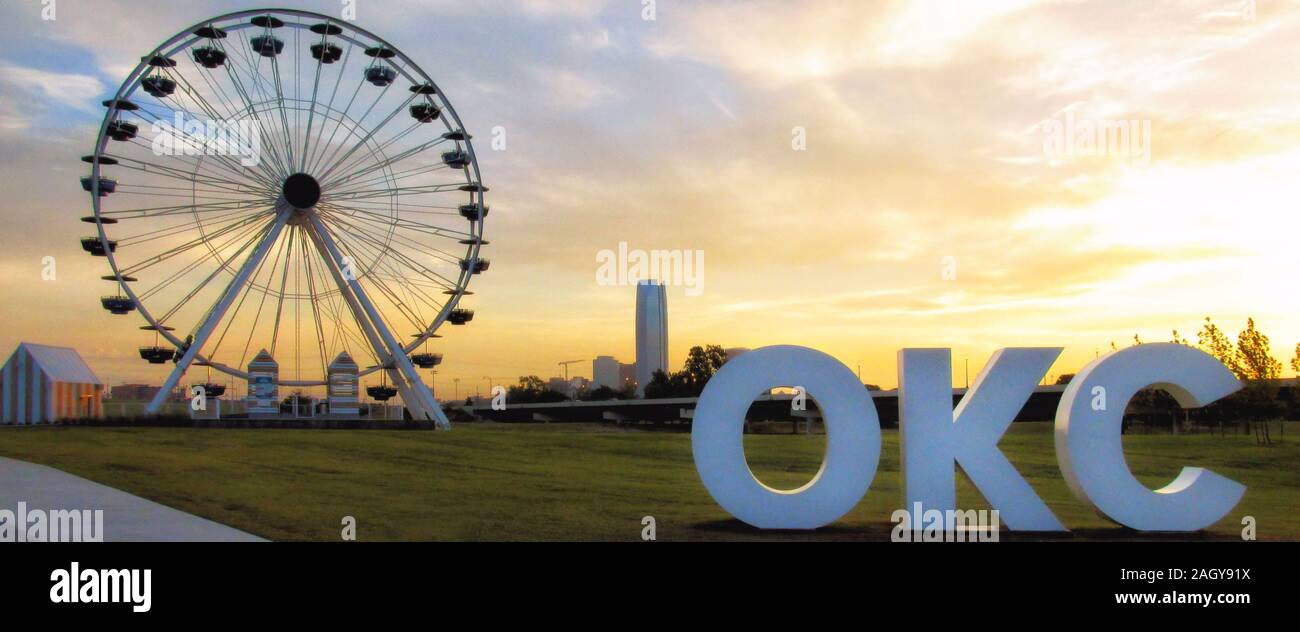 Wheeler Riesenrad und riesigen Schild stand out gegen einen Sonnenaufgang Himmel mit der Innenstadt von Oklahoma City im Hintergrund. Stockfoto